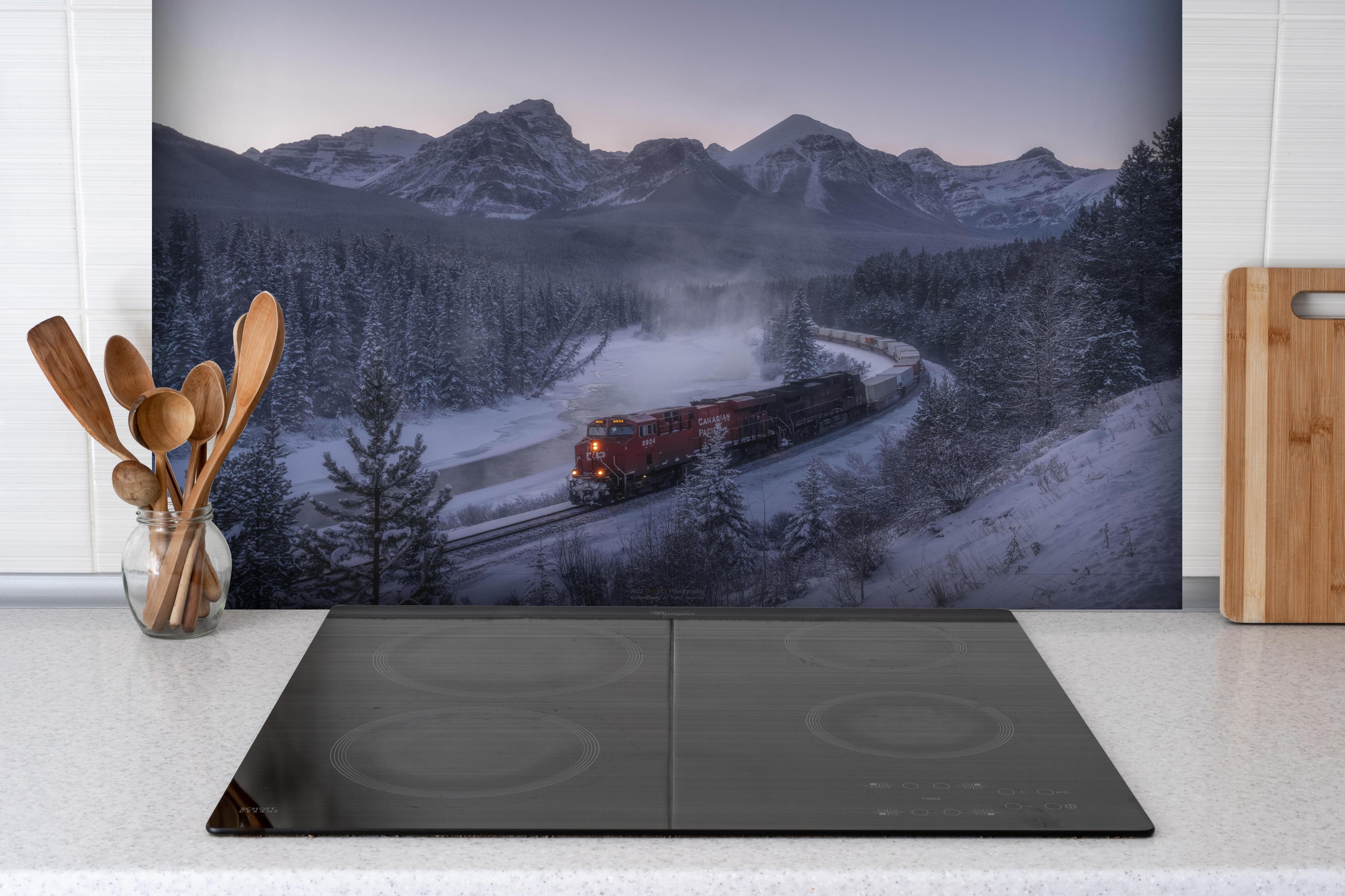 Spritzschutz - Roter Zug fährt durch verschneite Berglandschaft hinter einem Cerankochfeld zwischen Holz-Kochutensilien