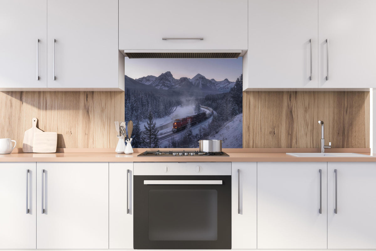 Spritzschutz - Roter Zug fährt durch verschneite Berglandschaft hinter einem Cerankochfeld zwischen Holz-Kochutensilien