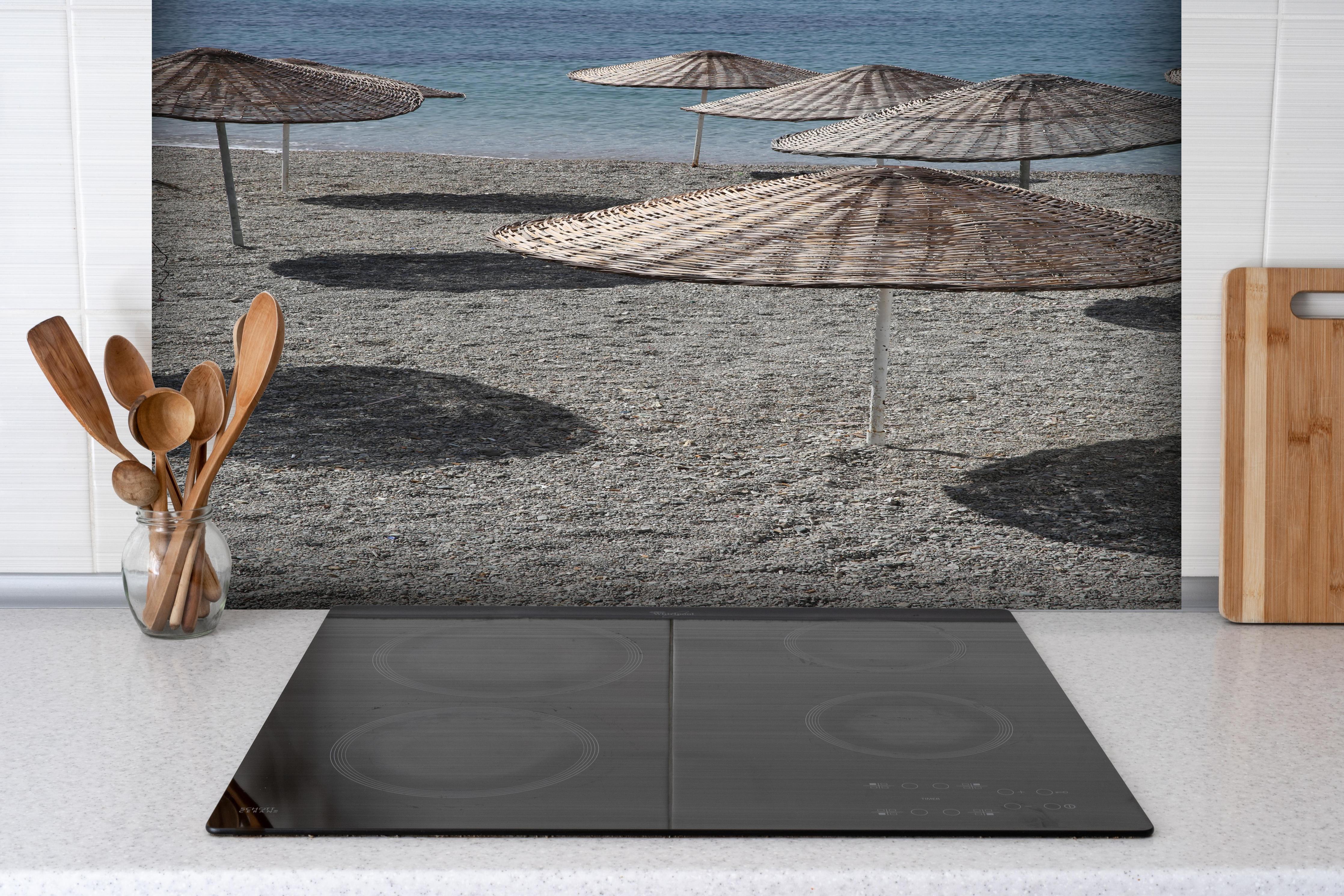 Spritzschutz - Ruhevolle Strandkulisse mit Sonnenschirmen hinter einem Cerankochfeld zwischen Holz-Kochutensilien