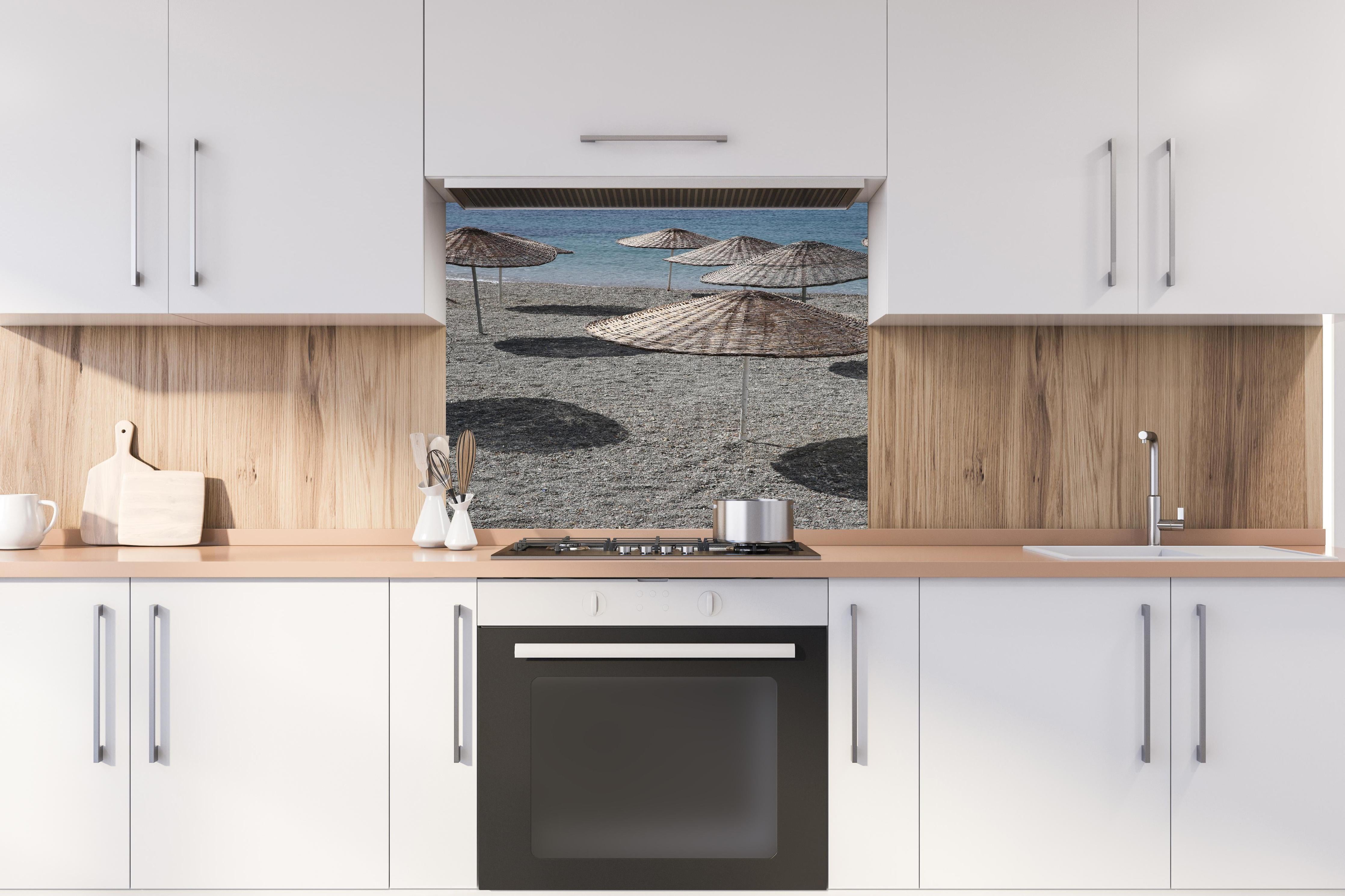Spritzschutz - Ruhevolle Strandkulisse mit Sonnenschirmen hinter einem Cerankochfeld zwischen Holz-Kochutensilien