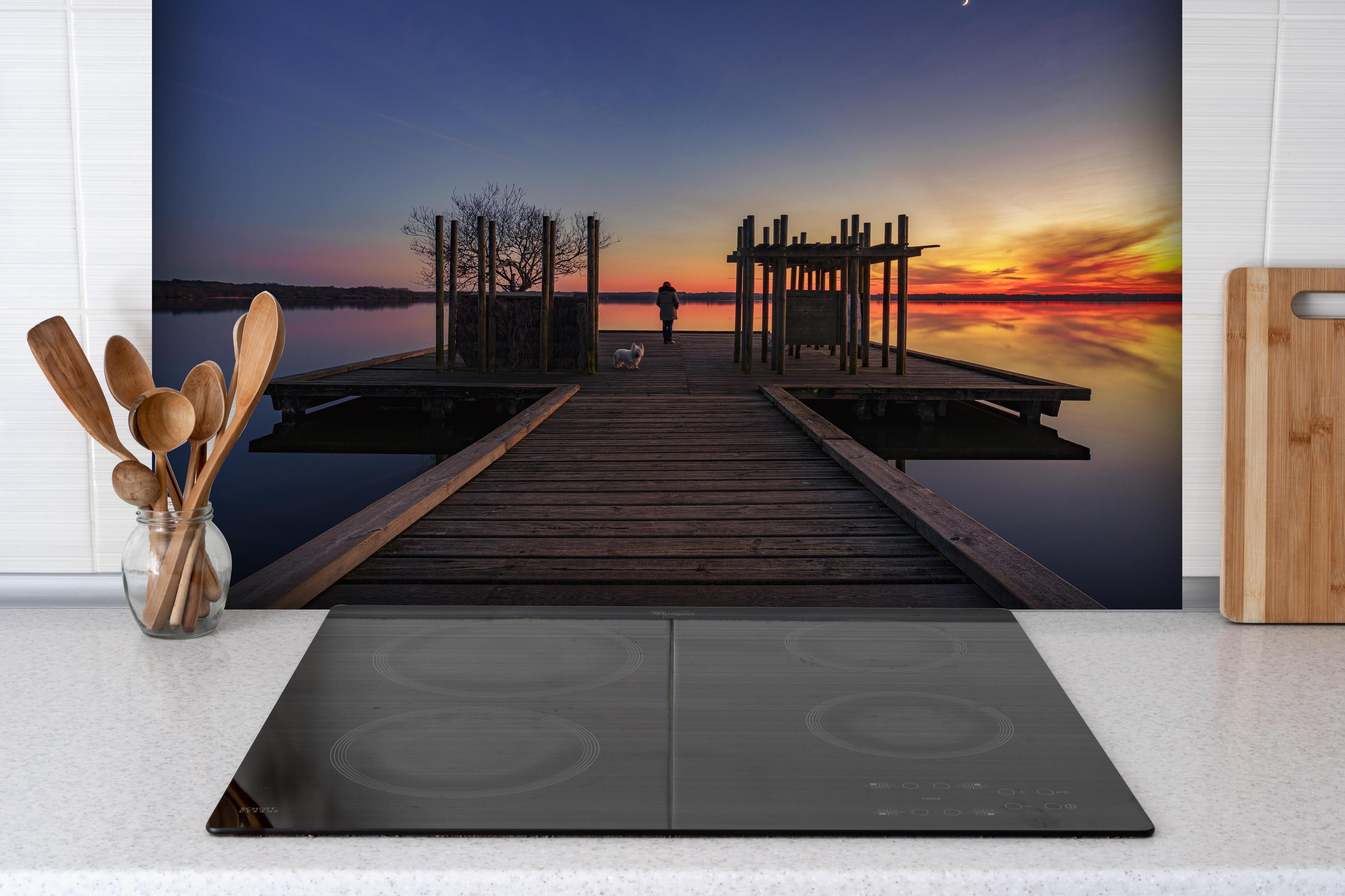 Spritzschutz - Ruhiger See bei Sonnenuntergang hinter einem Cerankochfeld zwischen Holz-Kochutensilien