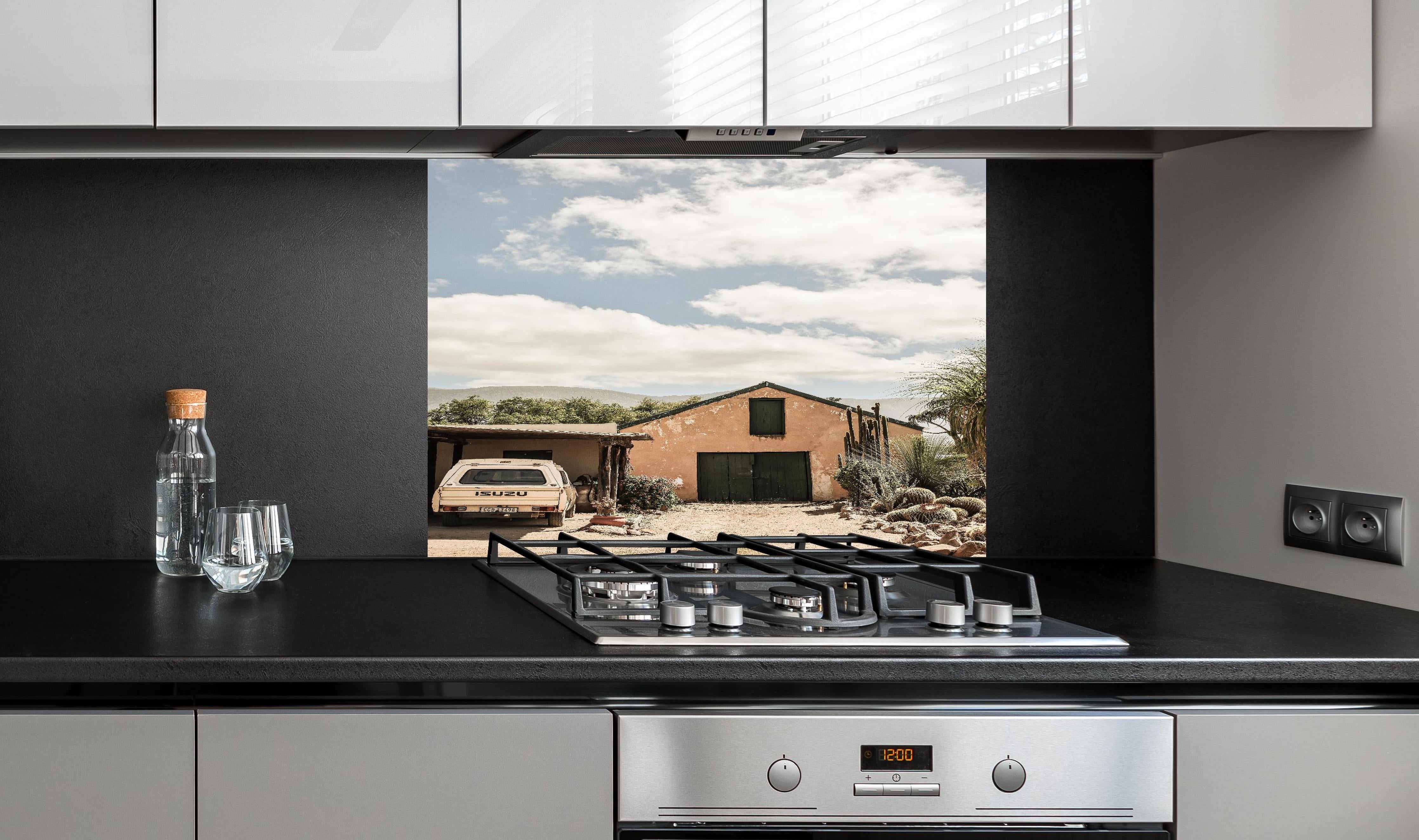 Spritzschutz - Rustikales Farmhaus Karoo in Ocker-Gelbtönen hinter einem Cerankochfeld zwischen Holz-Kochutensilien