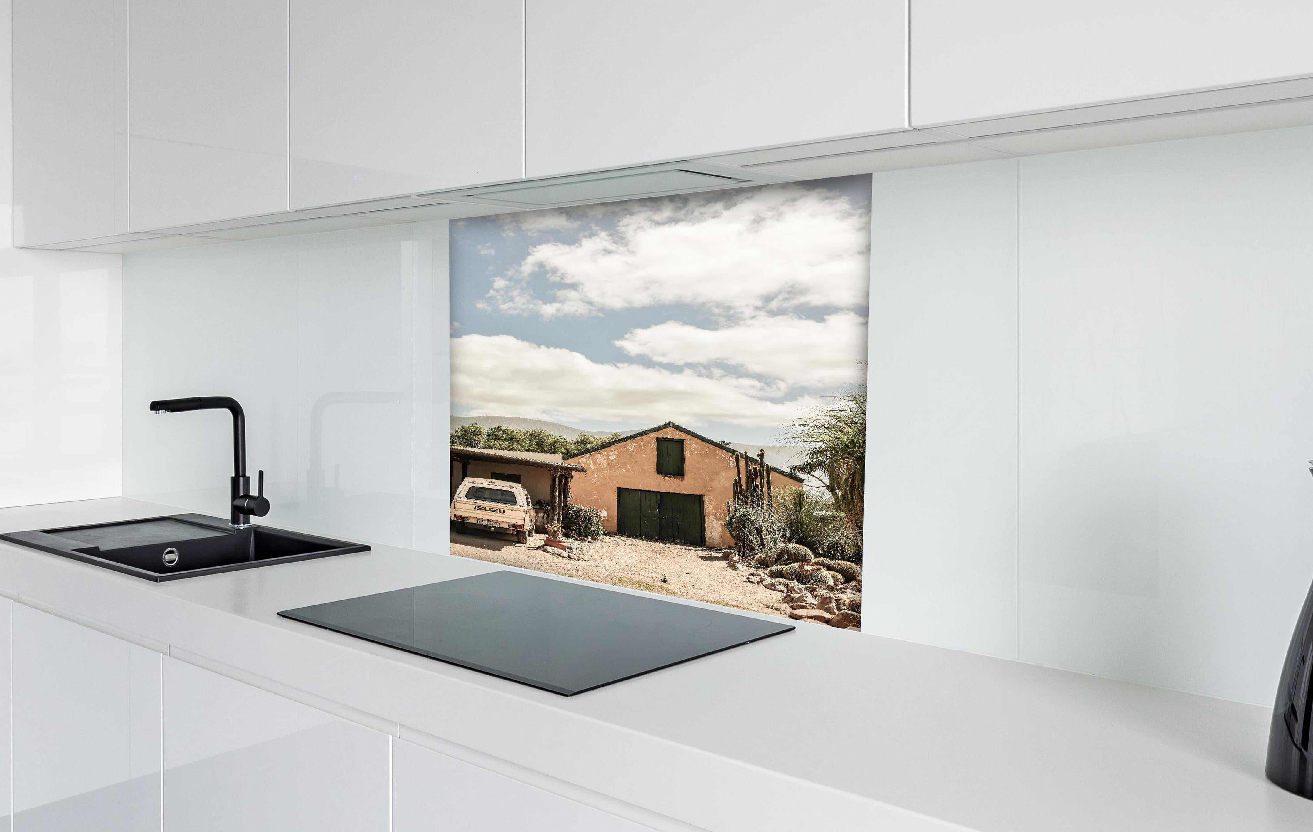 Spritzschutz - Rustikales Farmhaus Karoo in Ocker-Gelbtönen hinter einem Cerankochfeld zwischen Holz-Kochutensilien