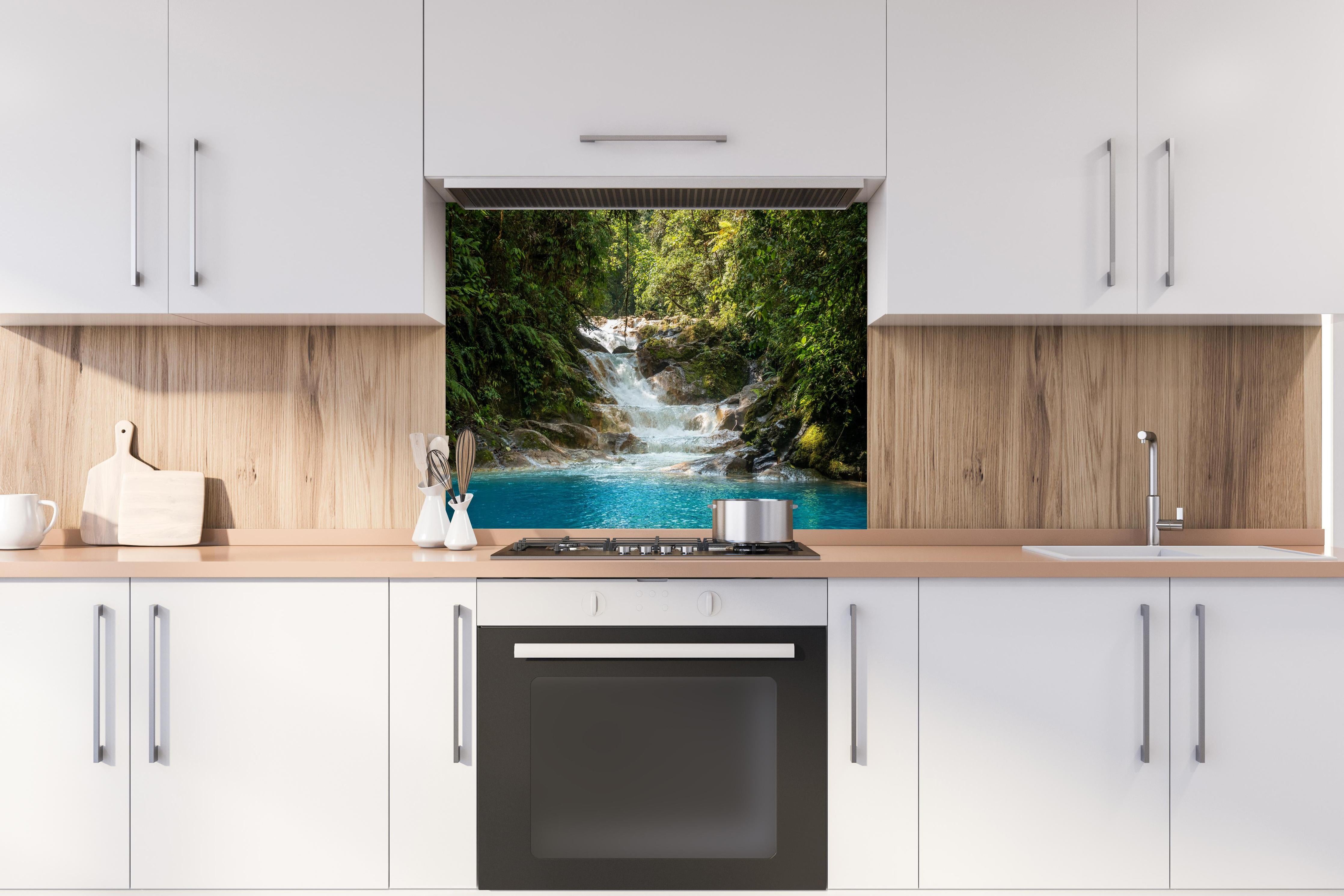 Spritzschutz - Sanfter Wasserfall im grünen Dschungel hinter einem Cerankochfeld zwischen Holz-Kochutensilien