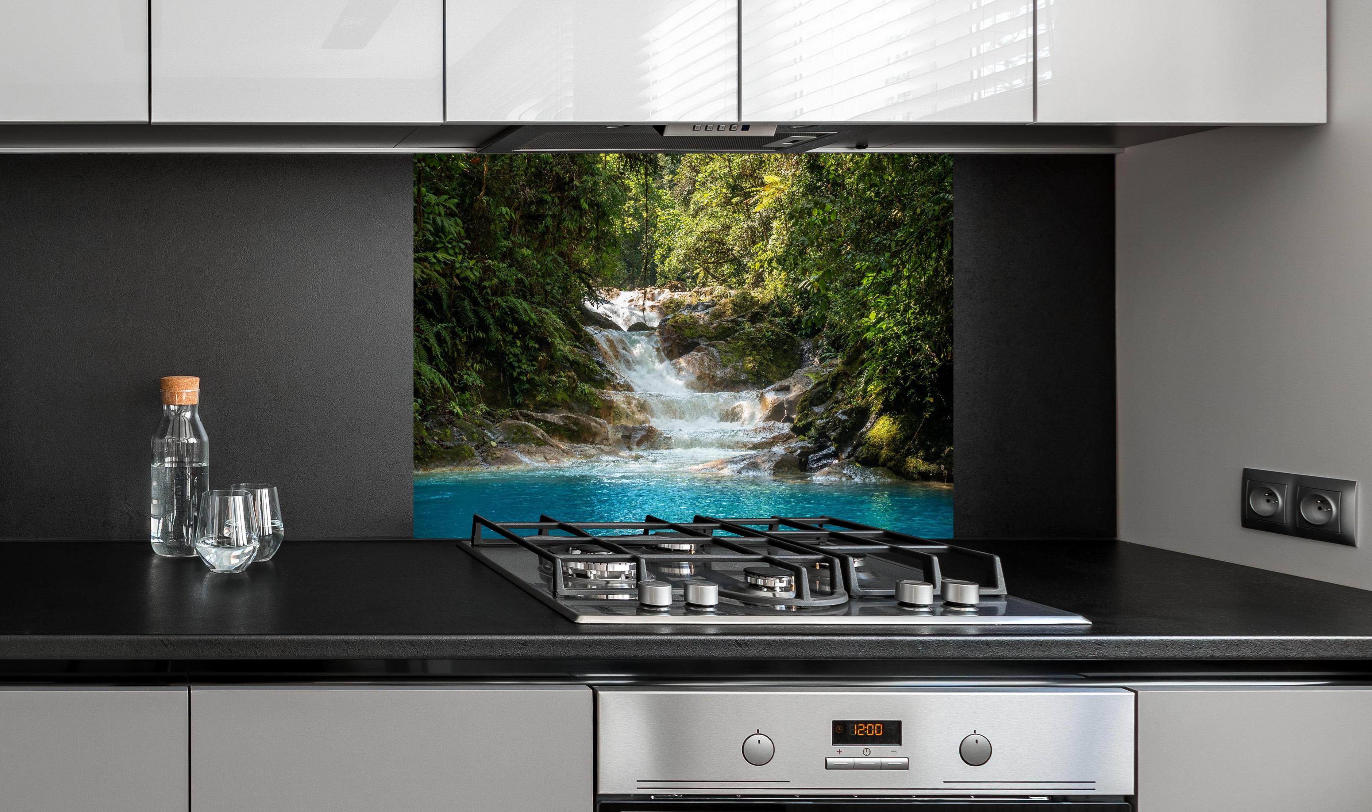 Spritzschutz - Sanfter Wasserfall im grünen Dschungel hinter einem Cerankochfeld zwischen Holz-Kochutensilien