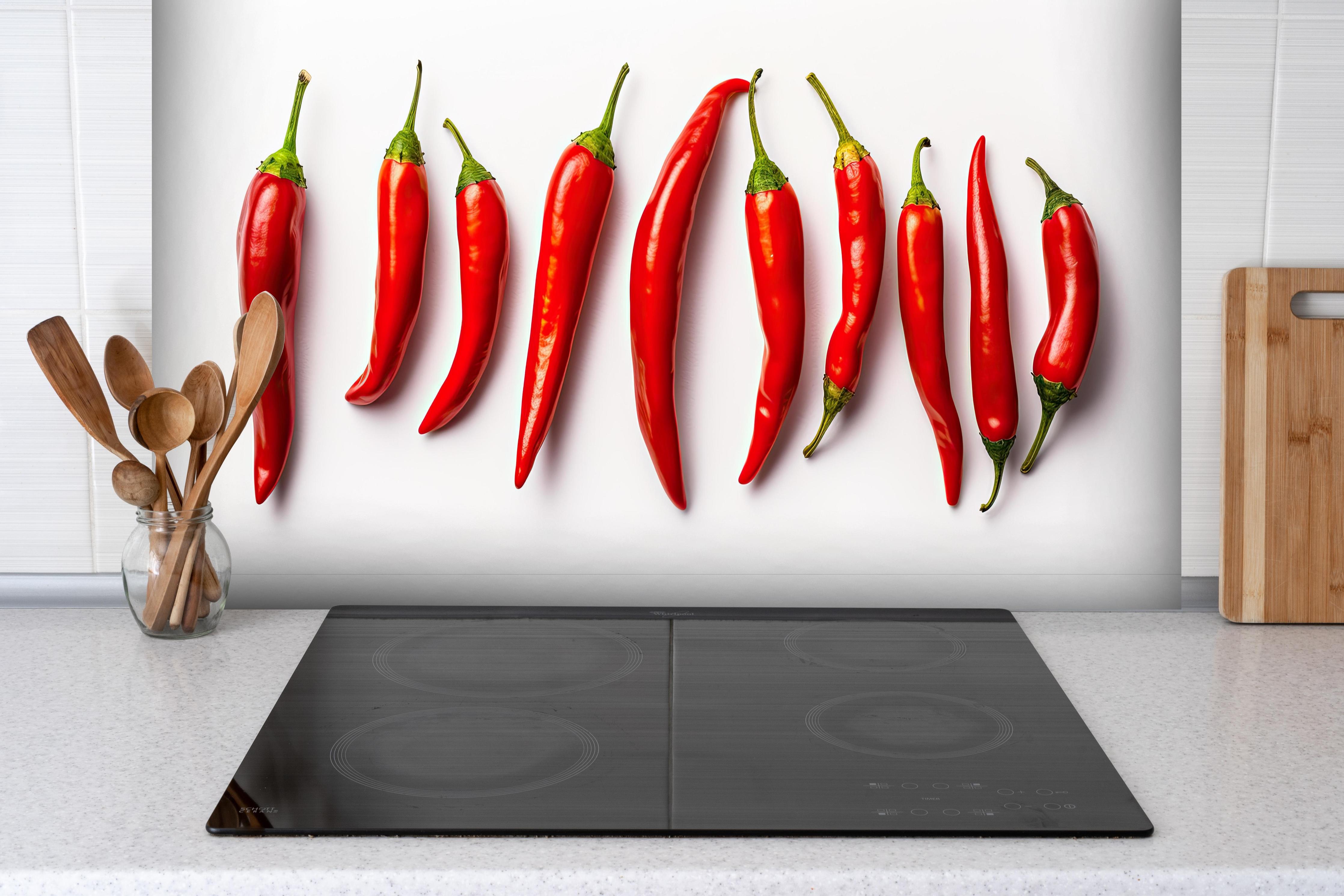 Spritzschutz - Scharfe Rote Chili Schoten im Überblick hinter einem Cerankochfeld zwischen Holz-Kochutensilien