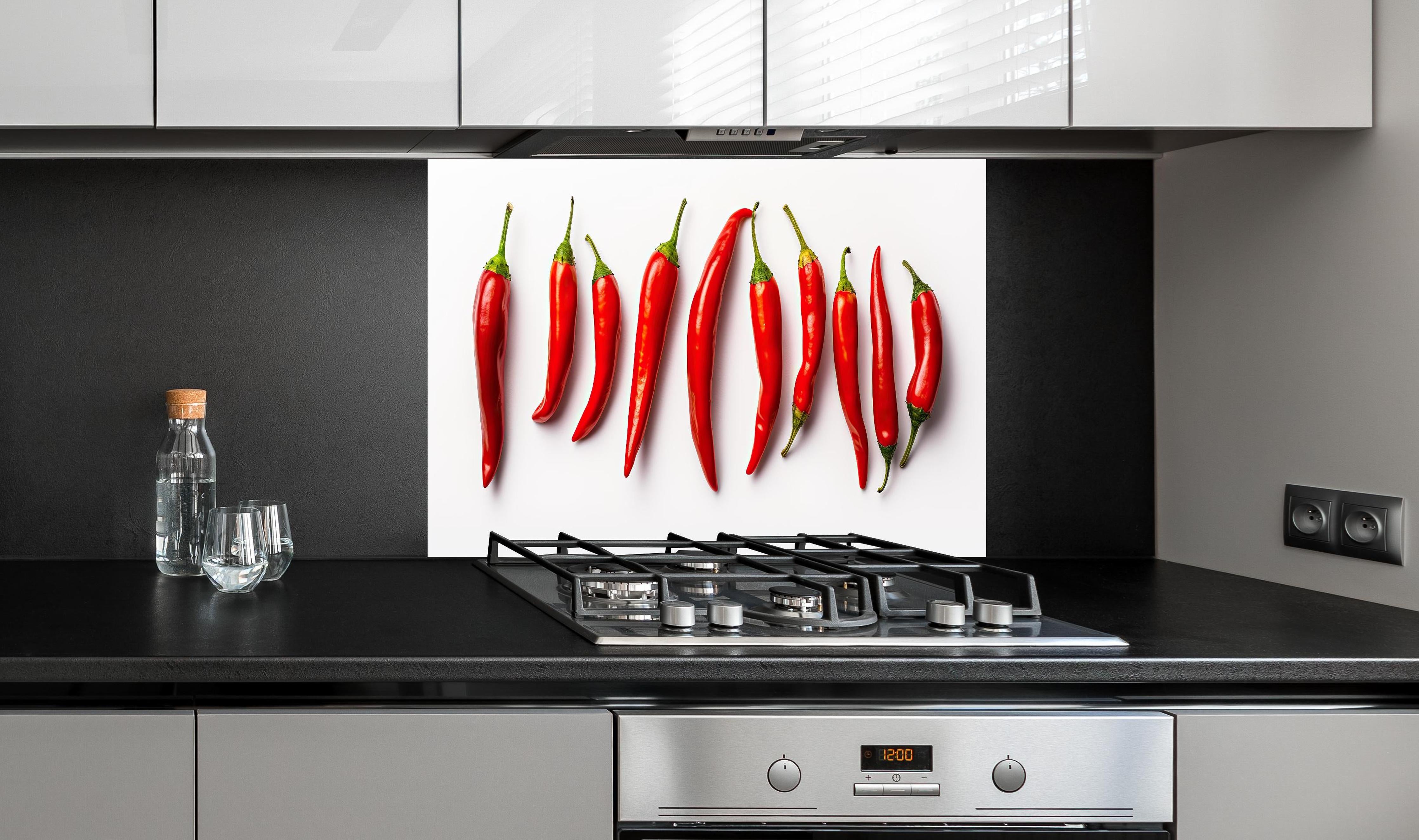 Spritzschutz - Scharfe Rote Chili Schoten im Überblick hinter einem Cerankochfeld zwischen Holz-Kochutensilien