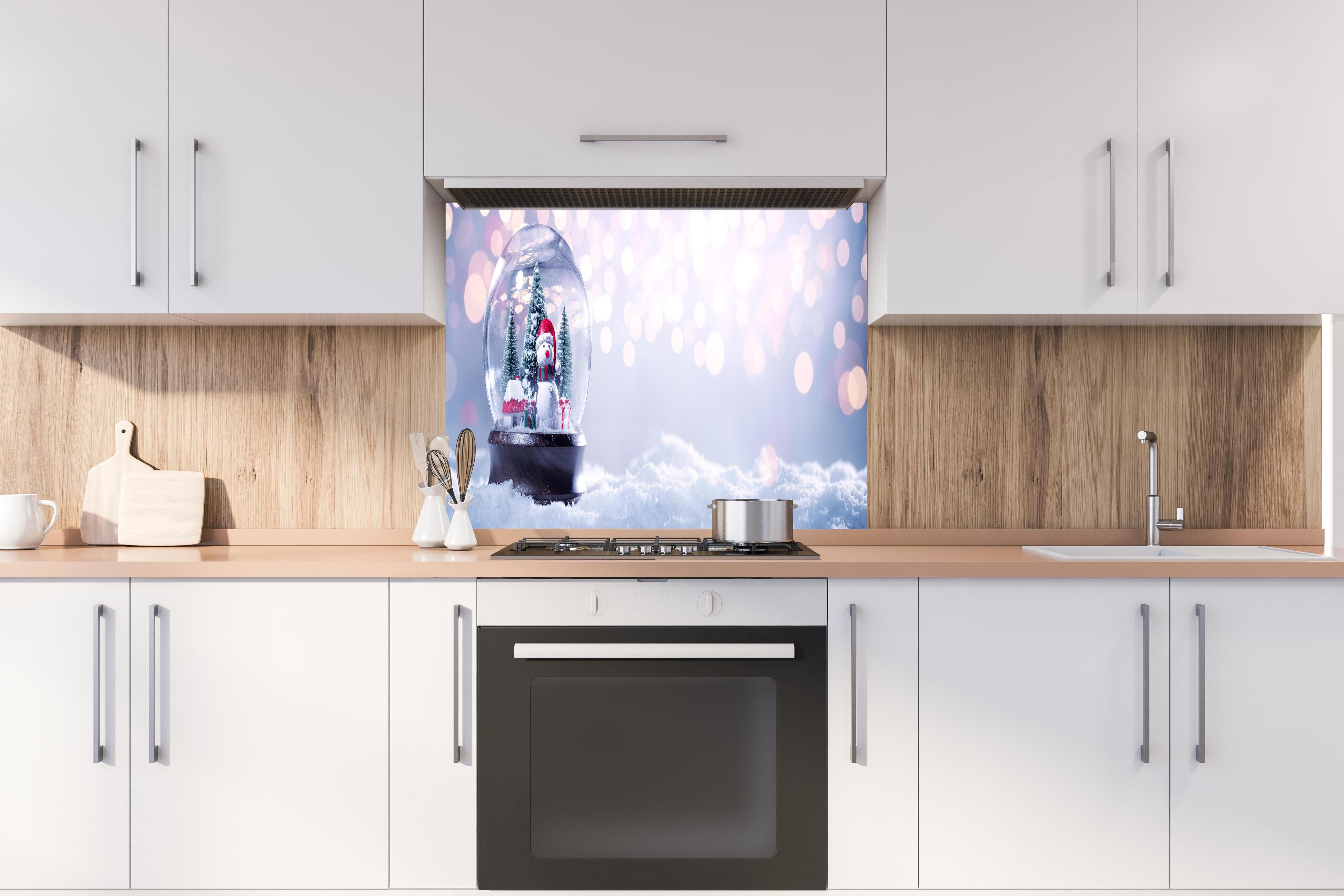 Spritzschutz - Schneekugel auf festlichem Hintergrund hinter einem Cerankochfeld zwischen Holz-Kochutensilien