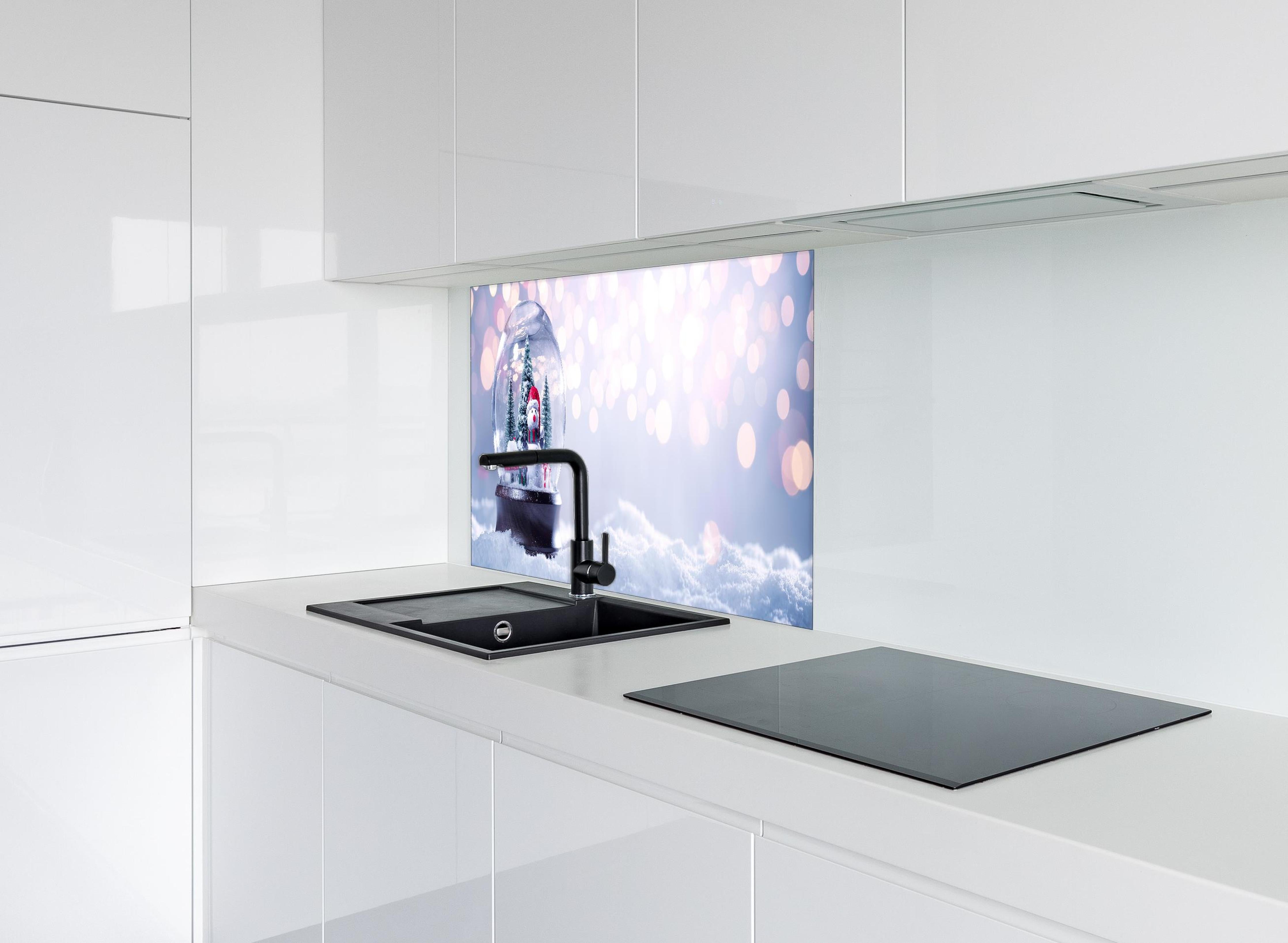 Spritzschutz - Schneekugel auf festlichem Hintergrund hinter einem Cerankochfeld zwischen Holz-Kochutensilien