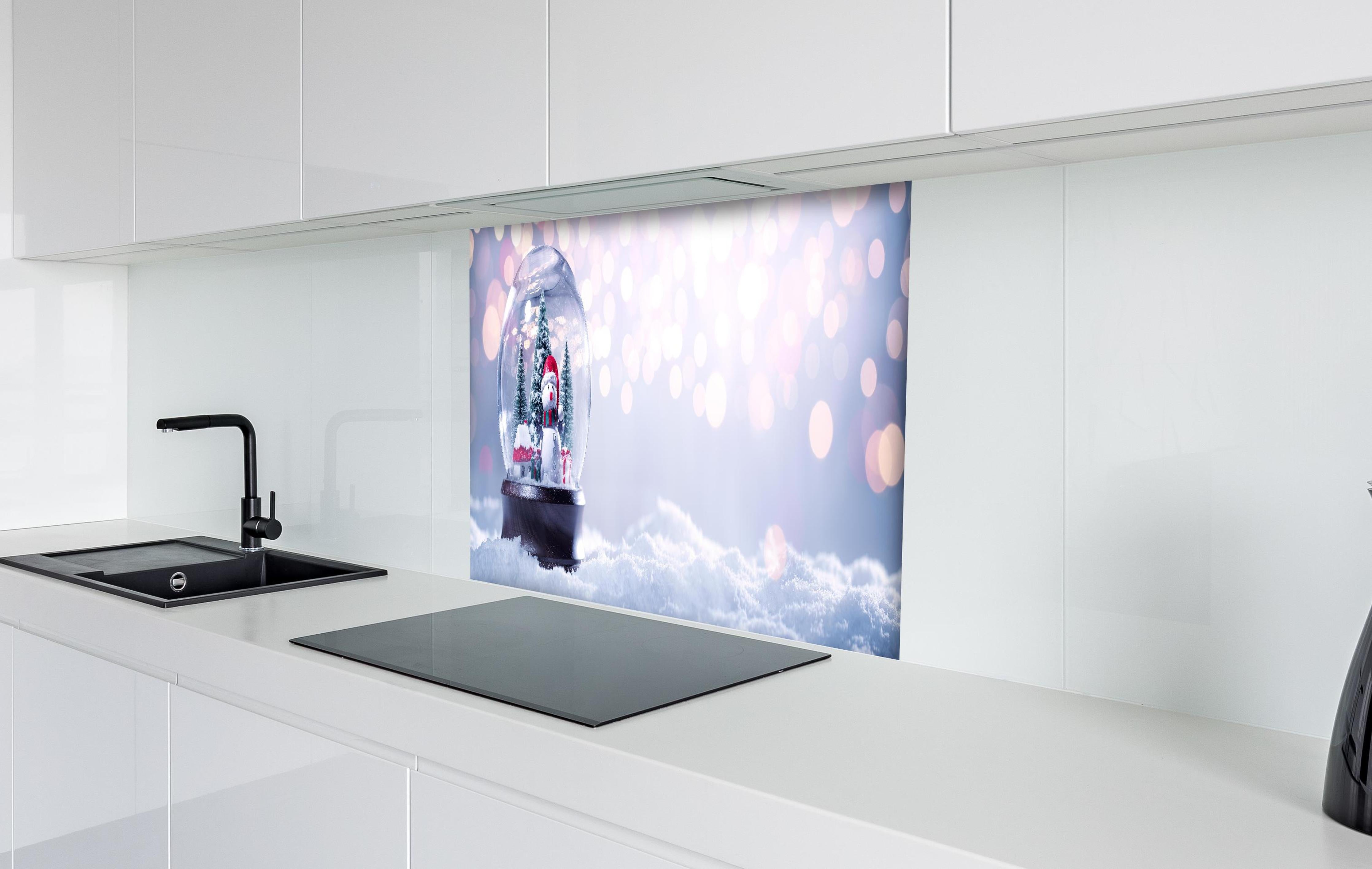 Spritzschutz - Schneekugel auf festlichem Hintergrund hinter einem Cerankochfeld zwischen Holz-Kochutensilien