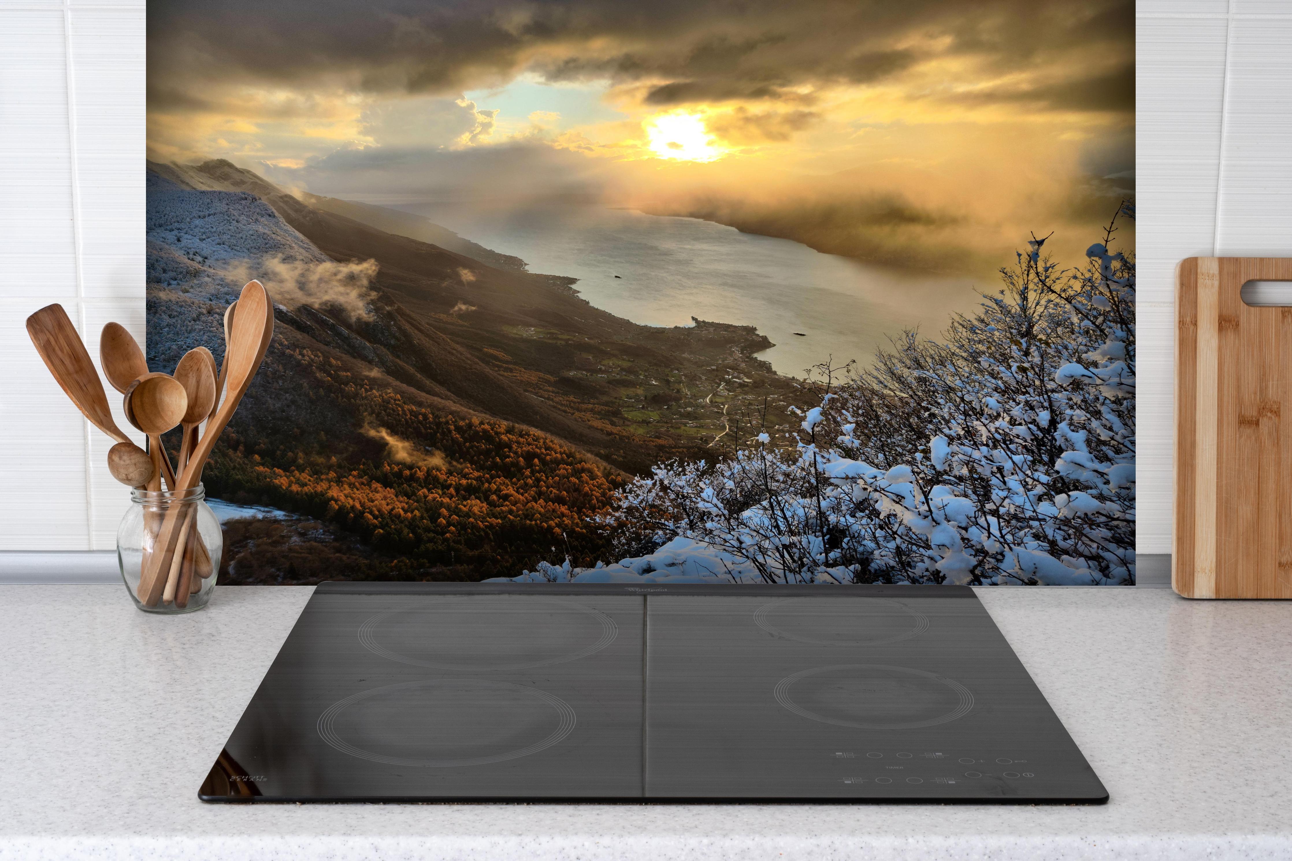 Spritzschutz - Schneelandschaft am Gardasee hinter einem Cerankochfeld zwischen Holz-Kochutensilien