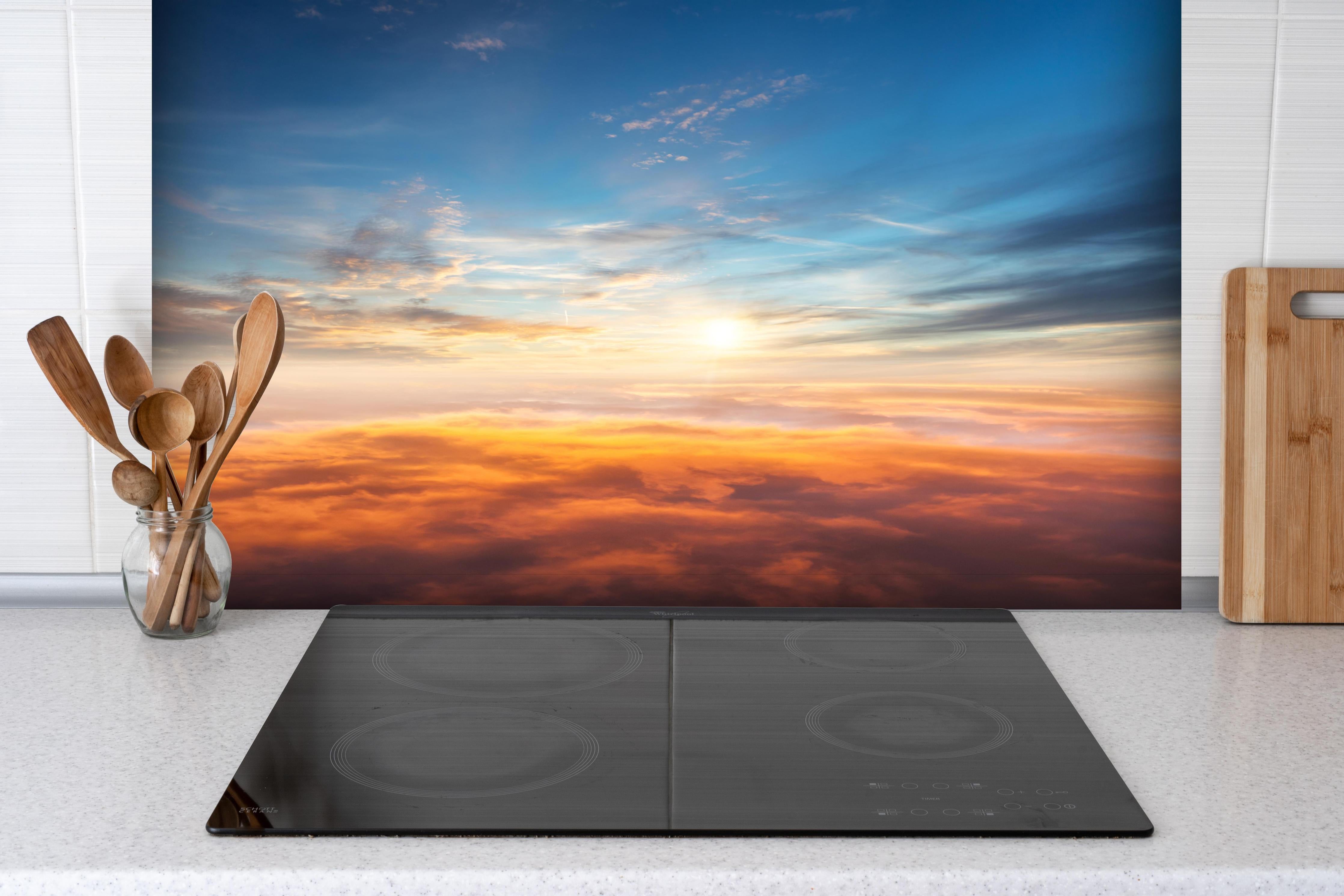 Spritzschutz - Schöner Sonnenuntergang über den Wolken hinter einem Cerankochfeld zwischen Holz-Kochutensilien
