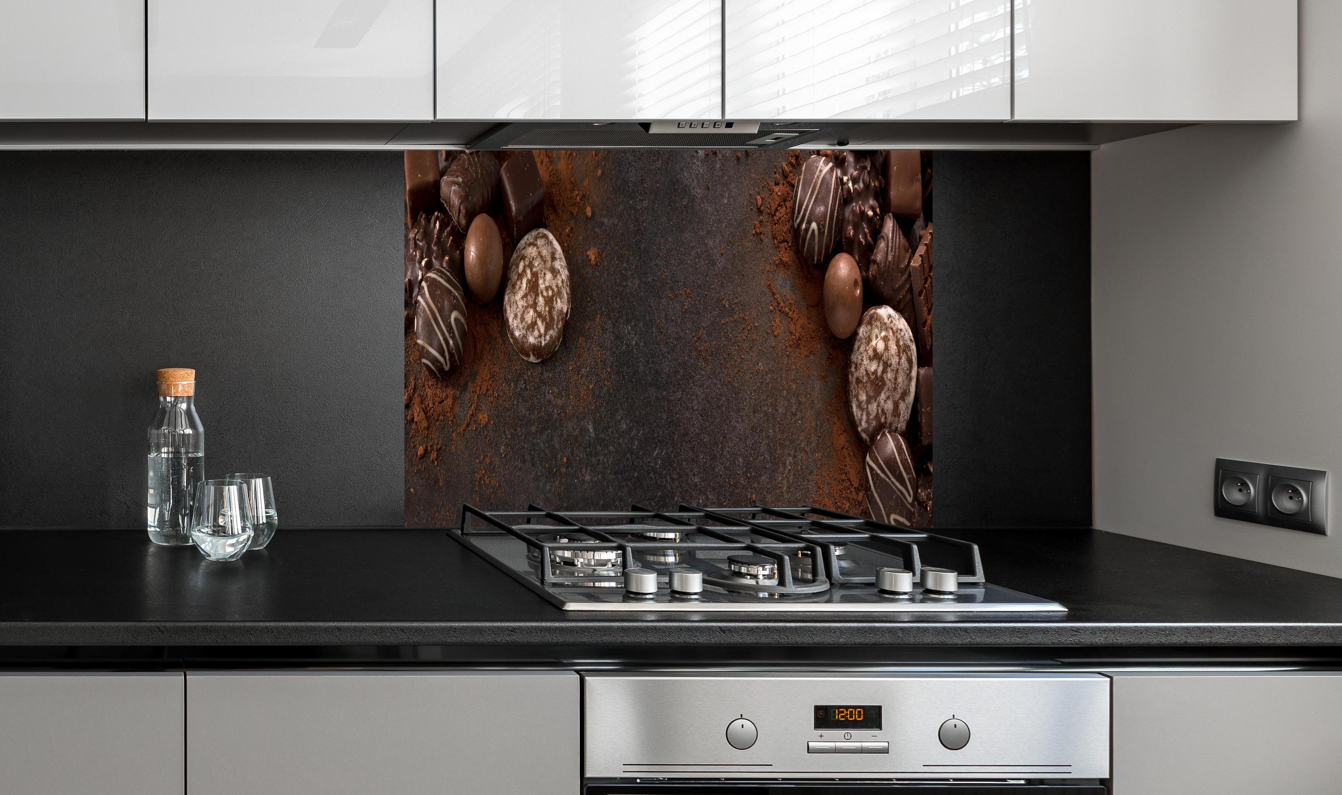 Spritzschutz - Schokoladenpralinen auf Schieferuntergrund hinter einem Cerankochfeld zwischen Holz-Kochutensilien