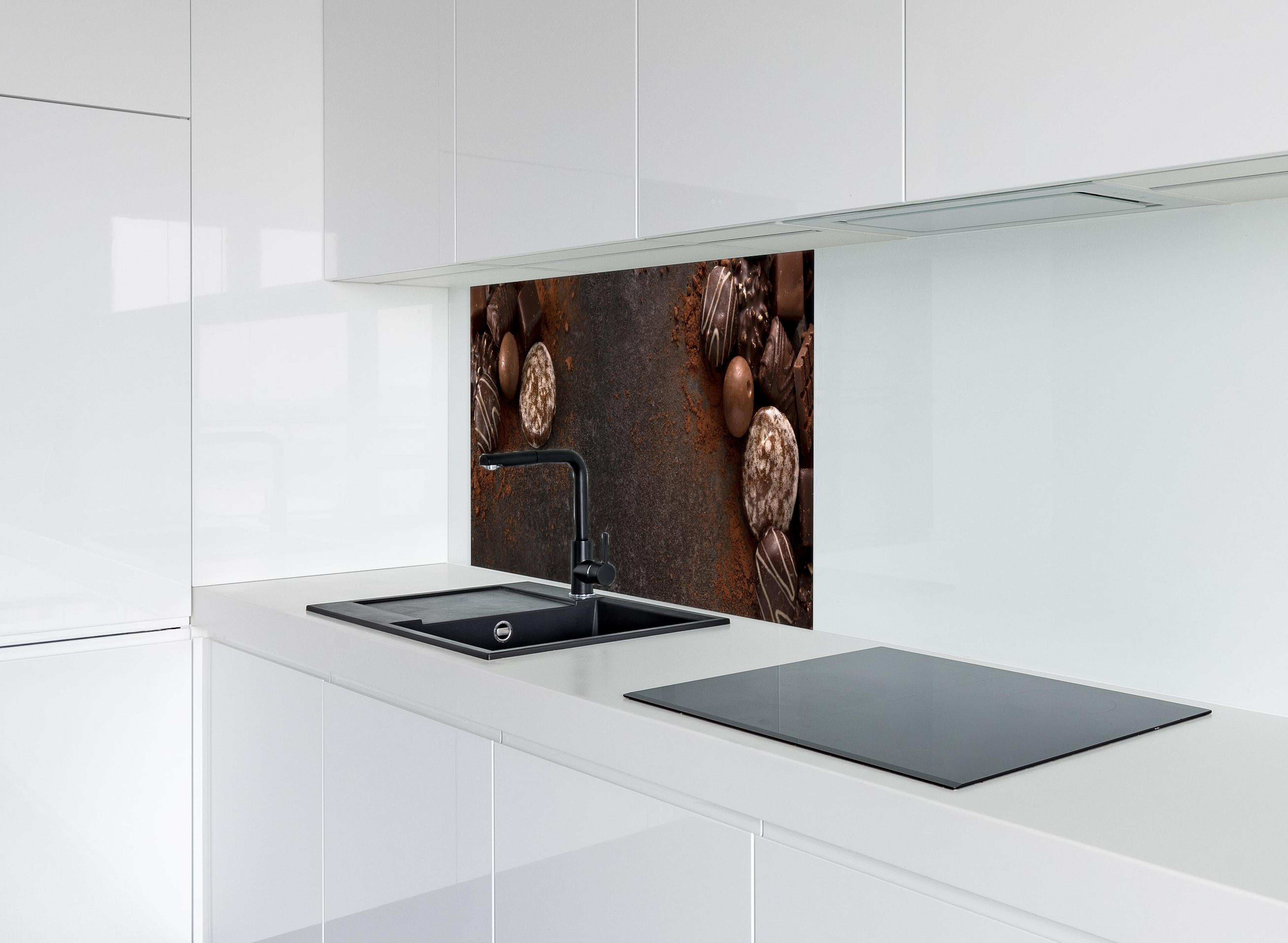 Spritzschutz - Schokoladenpralinen auf Schieferuntergrund hinter einem Cerankochfeld zwischen Holz-Kochutensilien