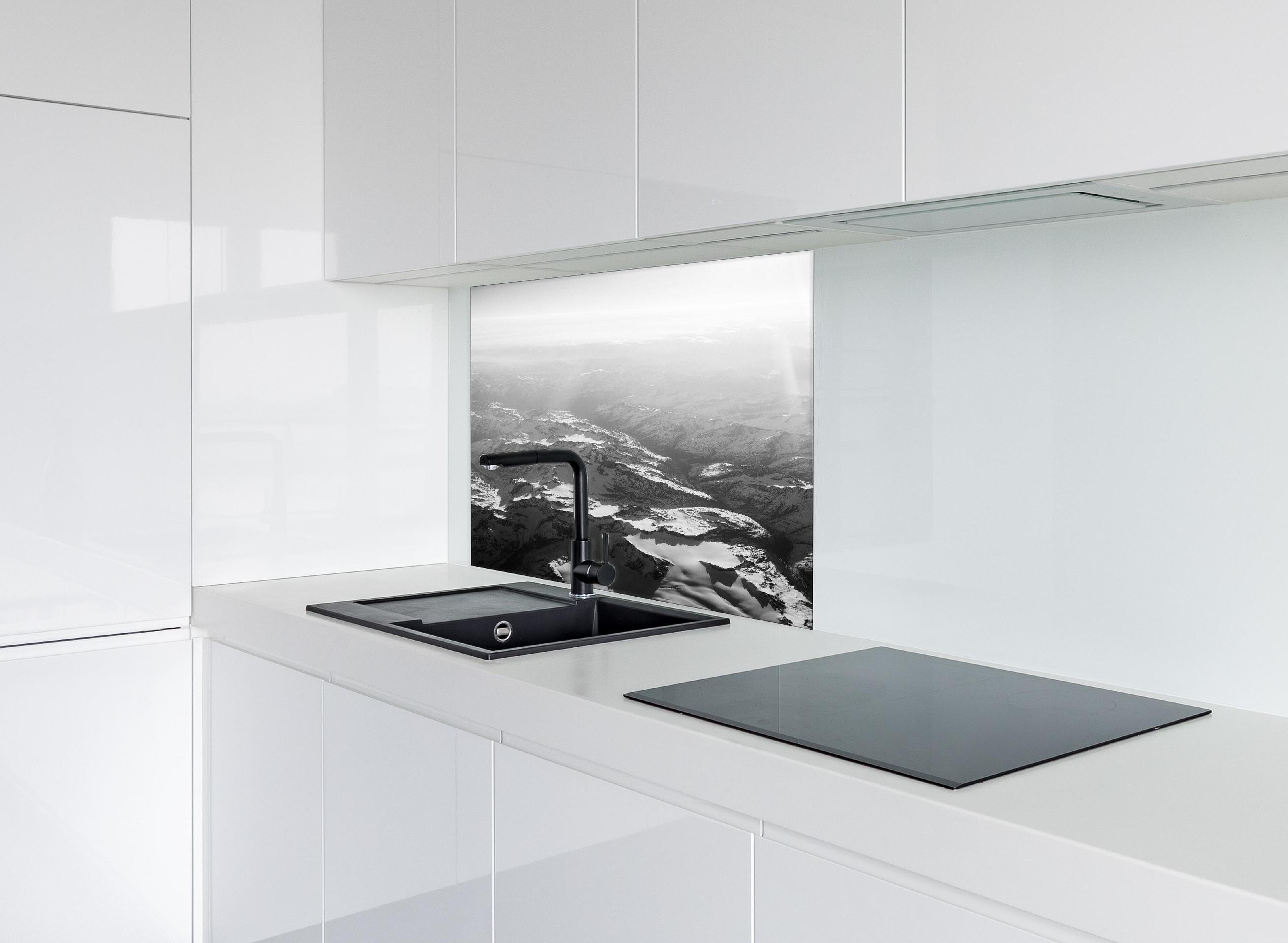 Spritzschutz - Schwarz-Weiß Fotografie Schneebedeckte Alpen hinter einem Cerankochfeld zwischen Holz-Kochutensilien