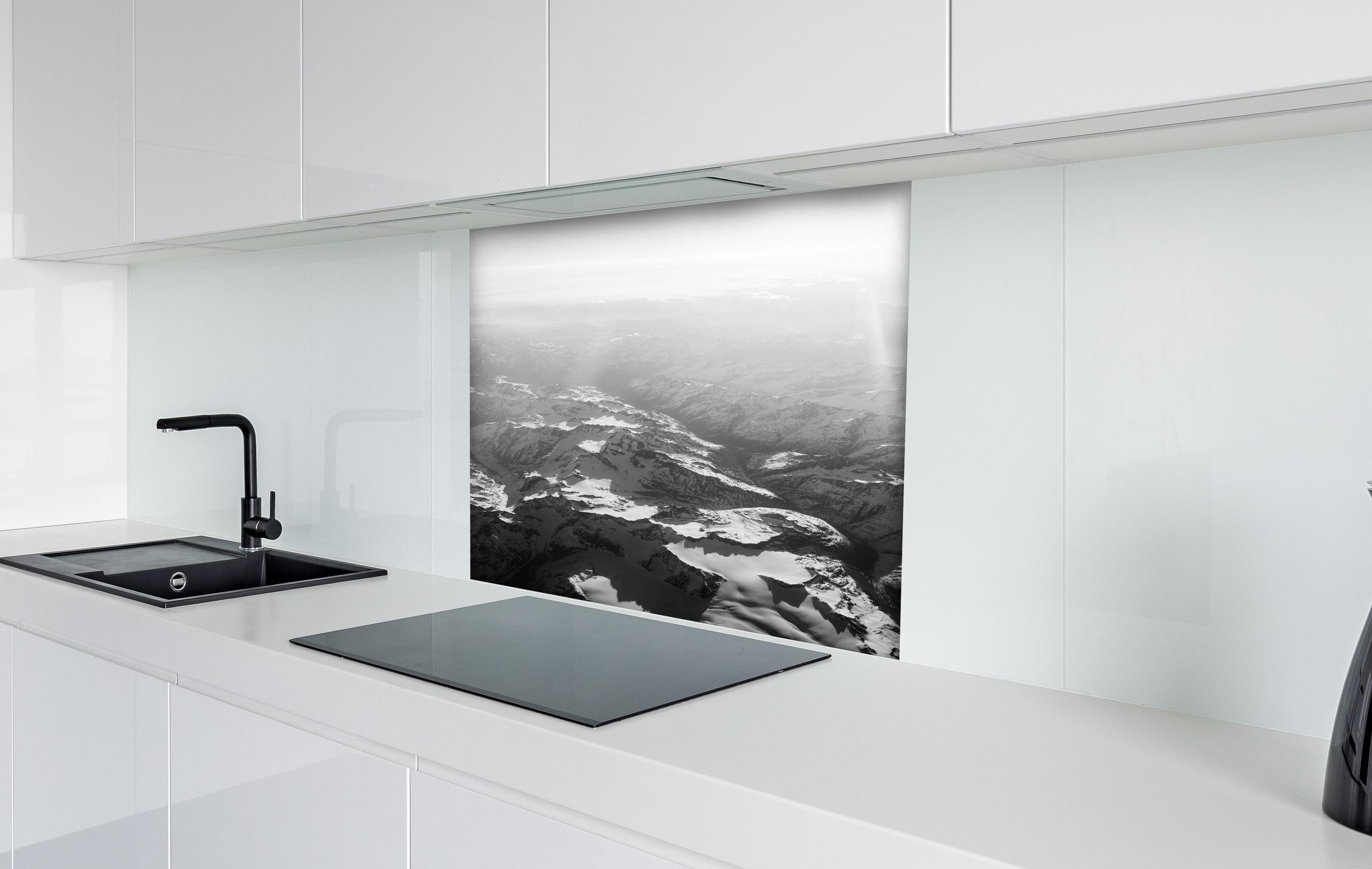 Spritzschutz - Schwarz-Weiß Fotografie Schneebedeckte Alpen hinter einem Cerankochfeld zwischen Holz-Kochutensilien