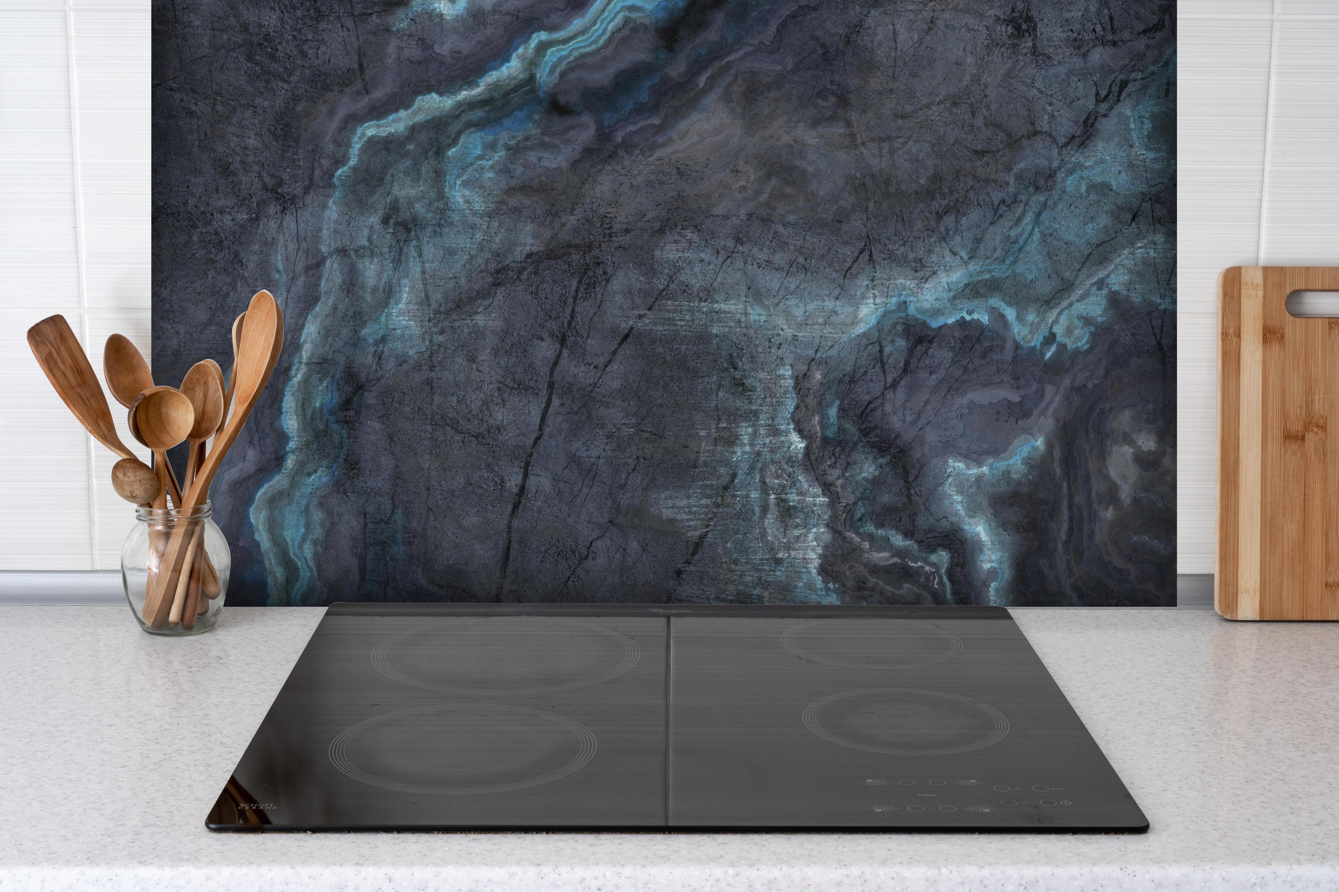 Spritzschutz - Schwarz-blauer Steinhintergrund hinter einem Cerankochfeld zwischen Holz-Kochutensilien