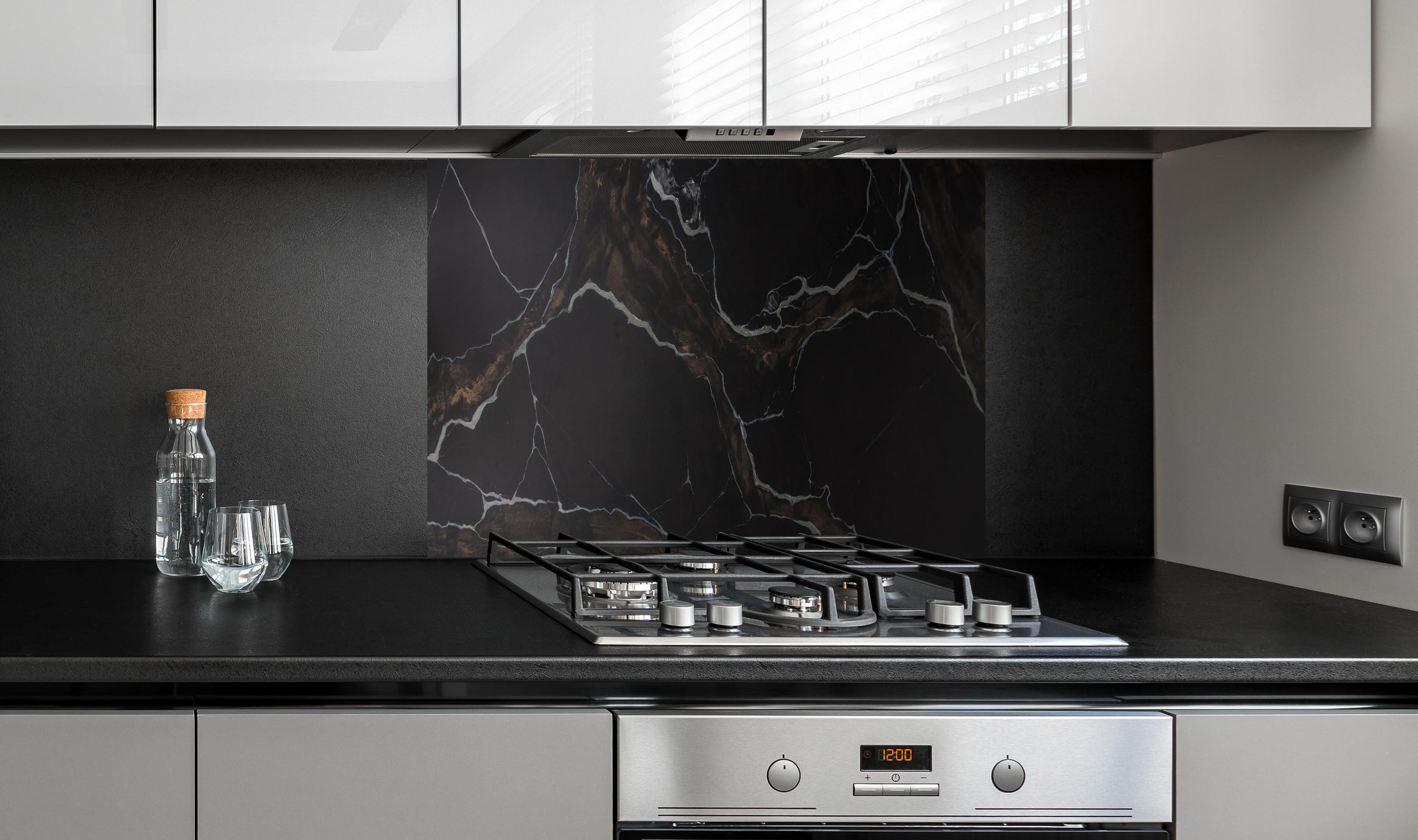 Spritzschutz - Schwarz-brauner Marmor hinter einem Cerankochfeld zwischen Holz-Kochutensilien