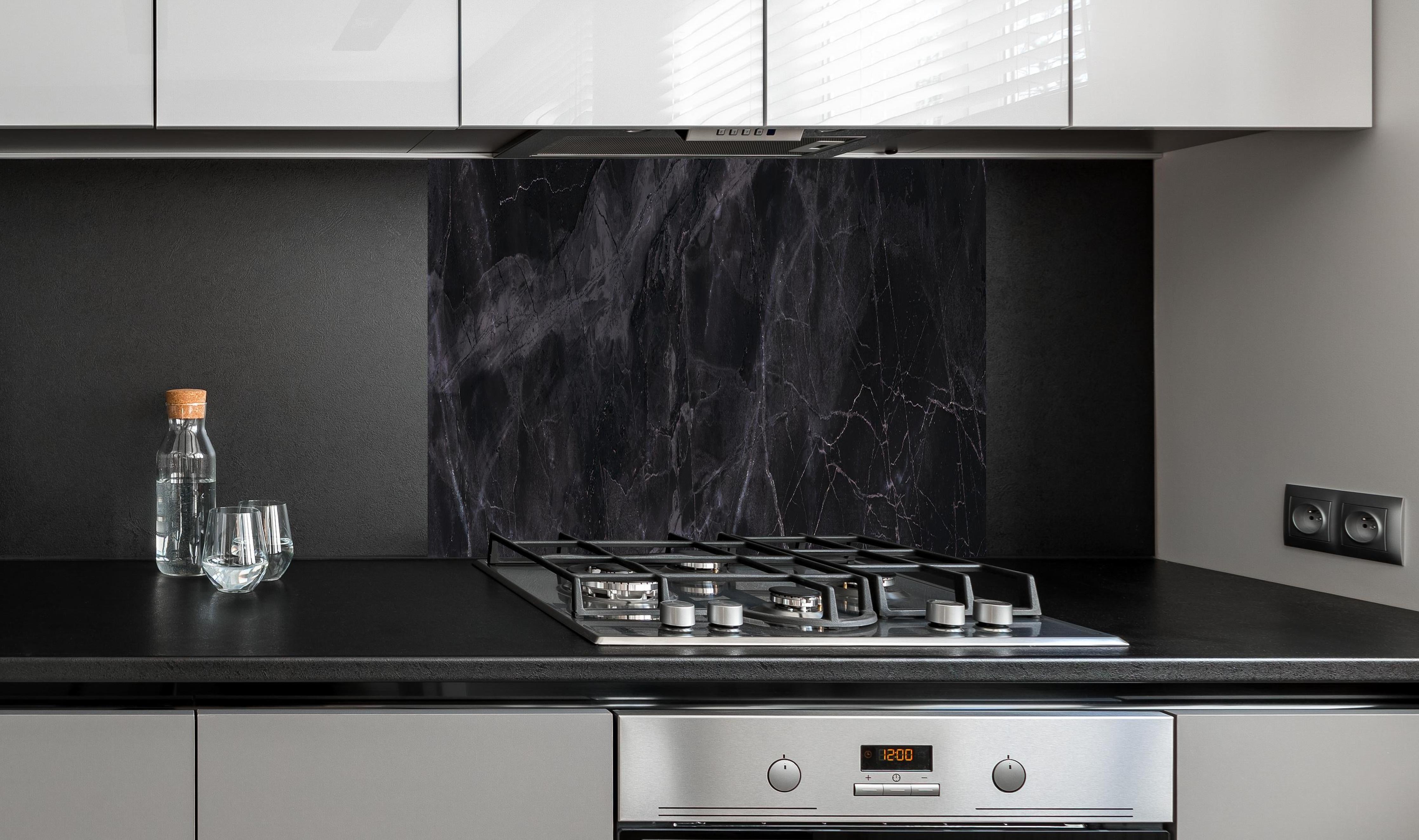 Spritzschutz - Schwarz-grauer Marmor hinter einem Cerankochfeld zwischen Holz-Kochutensilien