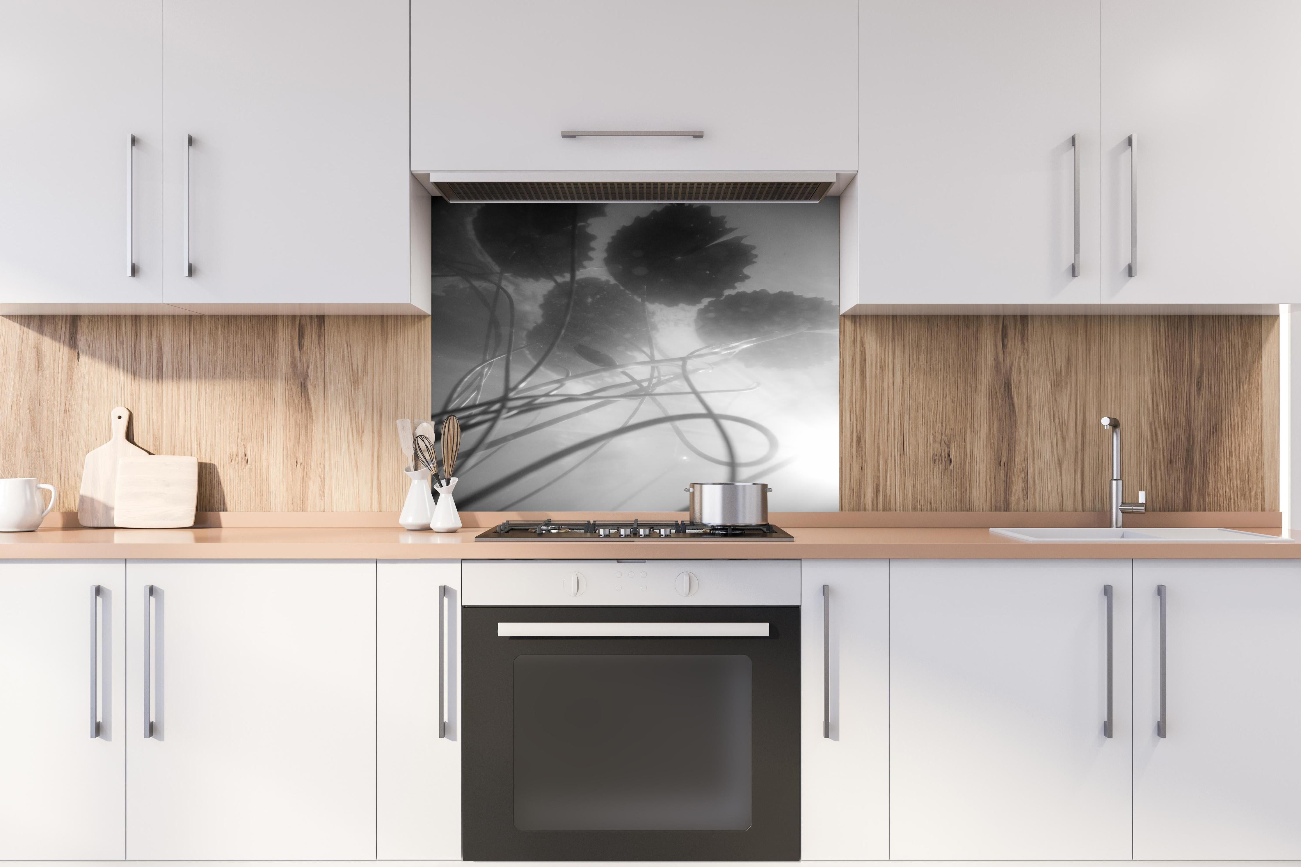 Spritzschutz - Schwarz-weiße Nahaufnahme der Water Lily hinter einem Cerankochfeld zwischen Holz-Kochutensilien