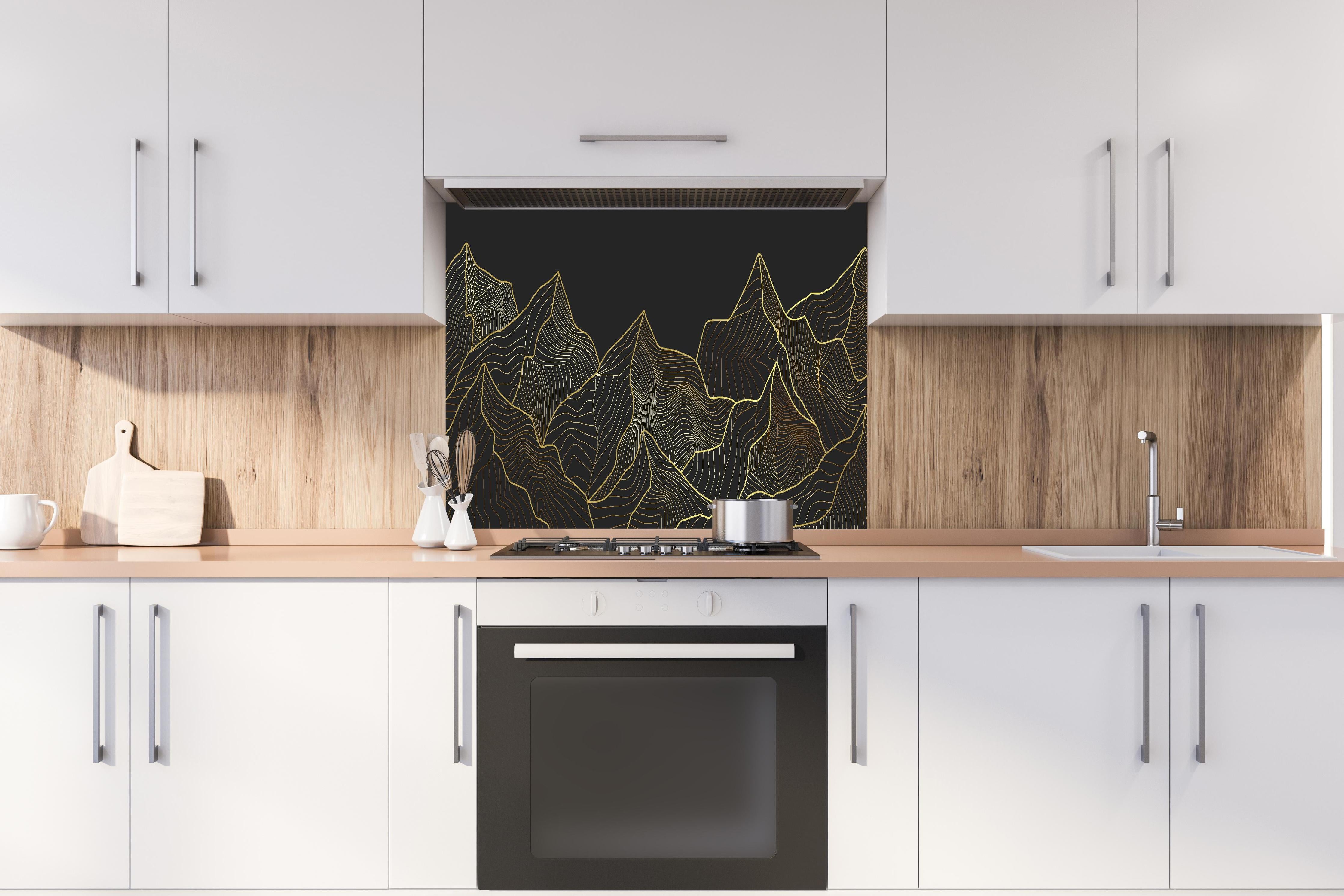 Spritzschutz - Schwarze Berge mit goldener Linienkunst hinter einem Cerankochfeld zwischen Holz-Kochutensilien