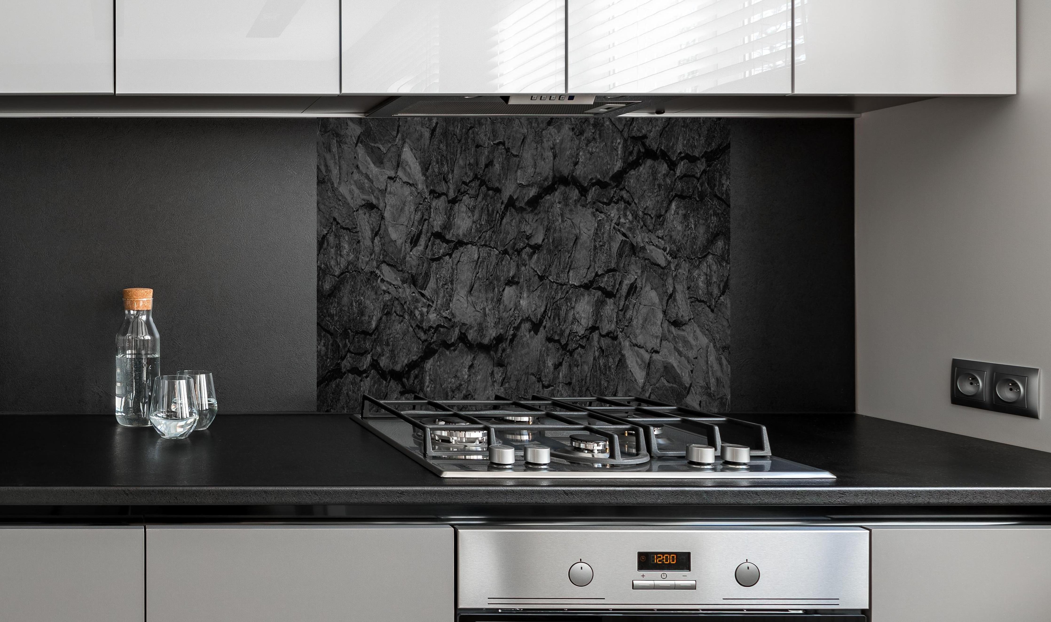 Spritzschutz - Schwarze Gesteinstextur mit Rissen hinter einem Cerankochfeld zwischen Holz-Kochutensilien