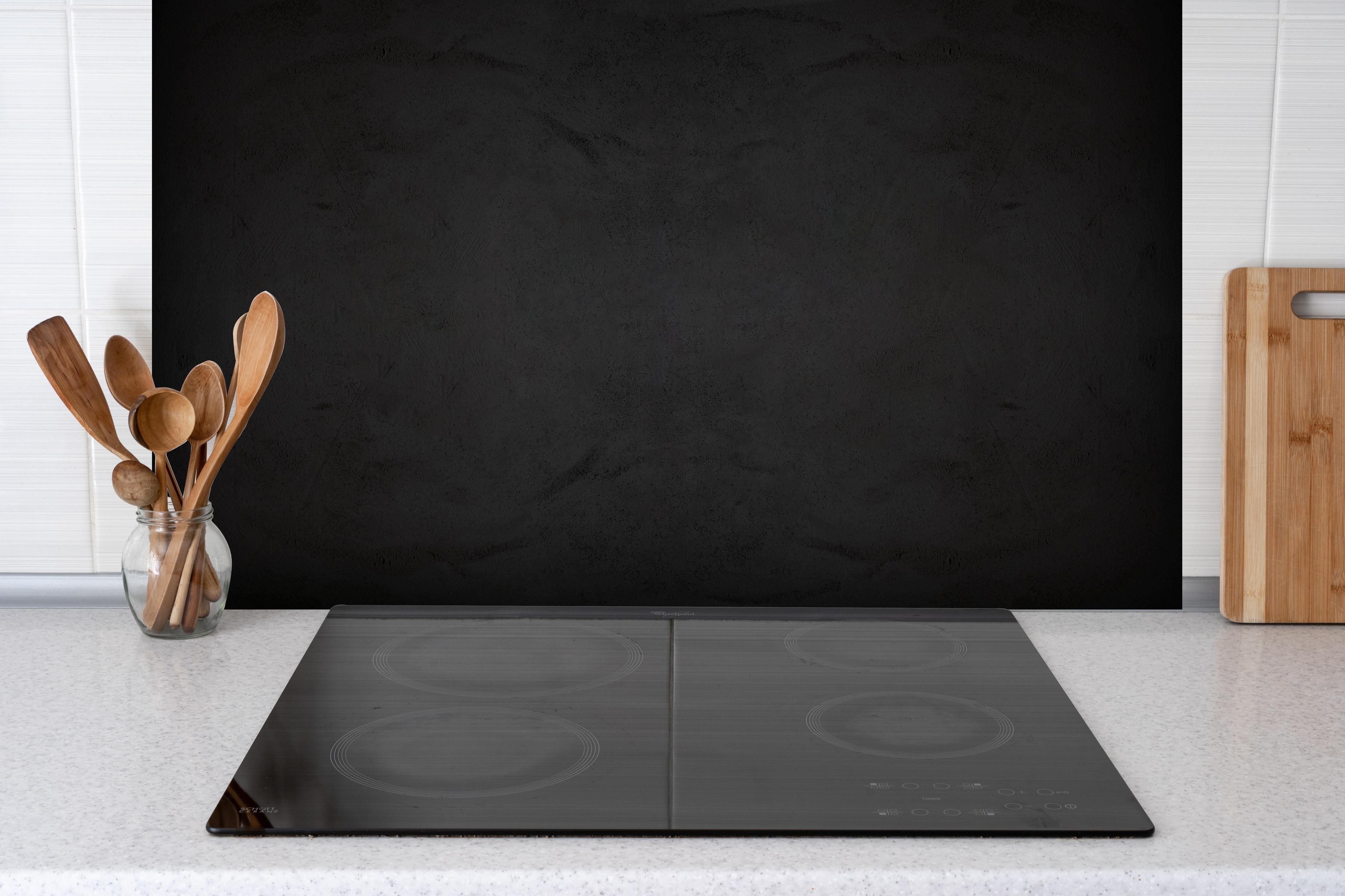 Spritzschutz - Schwarze anthrazit Textur hinter einem Cerankochfeld zwischen Holz-Kochutensilien