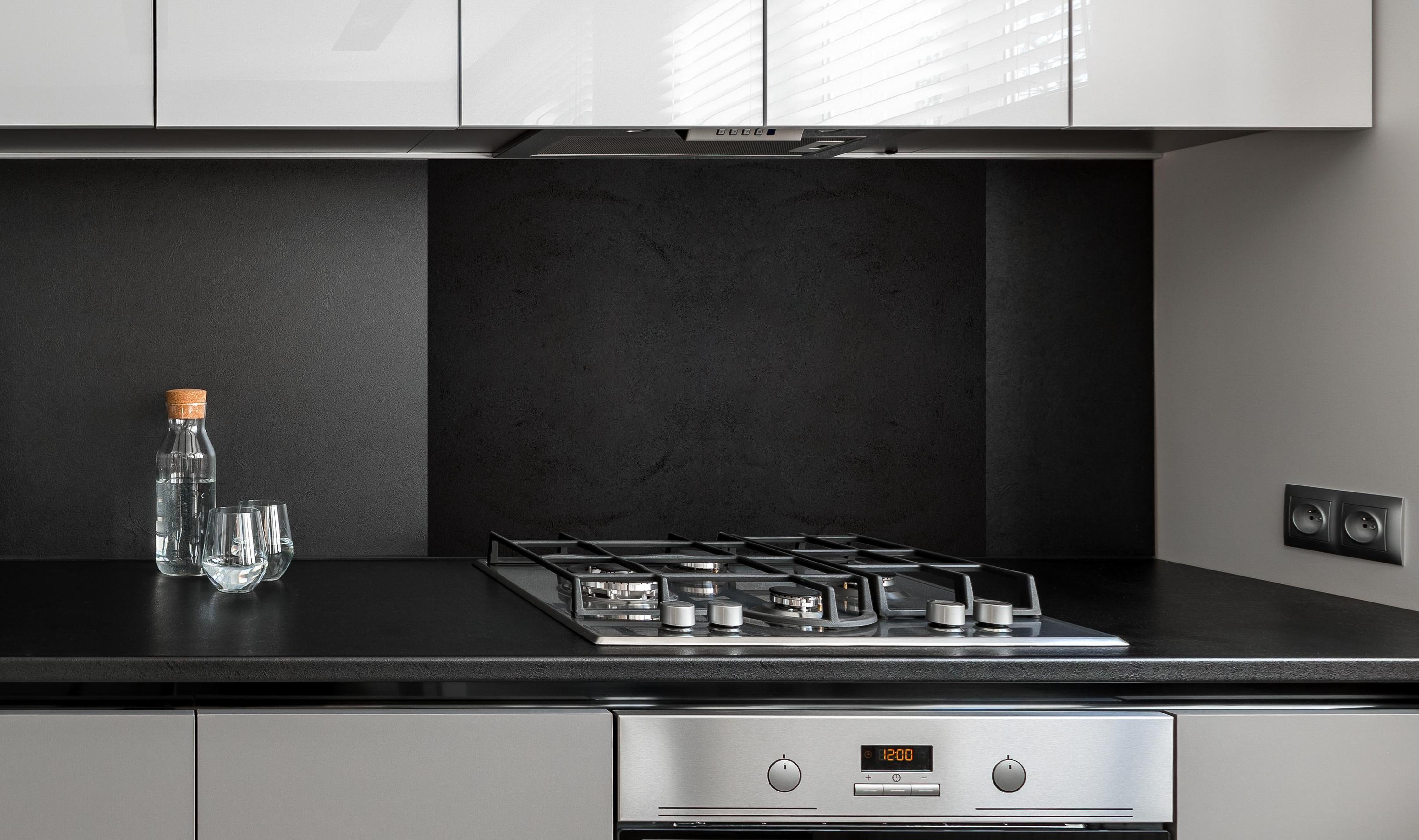 Spritzschutz - Schwarze anthrazit Textur hinter einem Cerankochfeld zwischen Holz-Kochutensilien