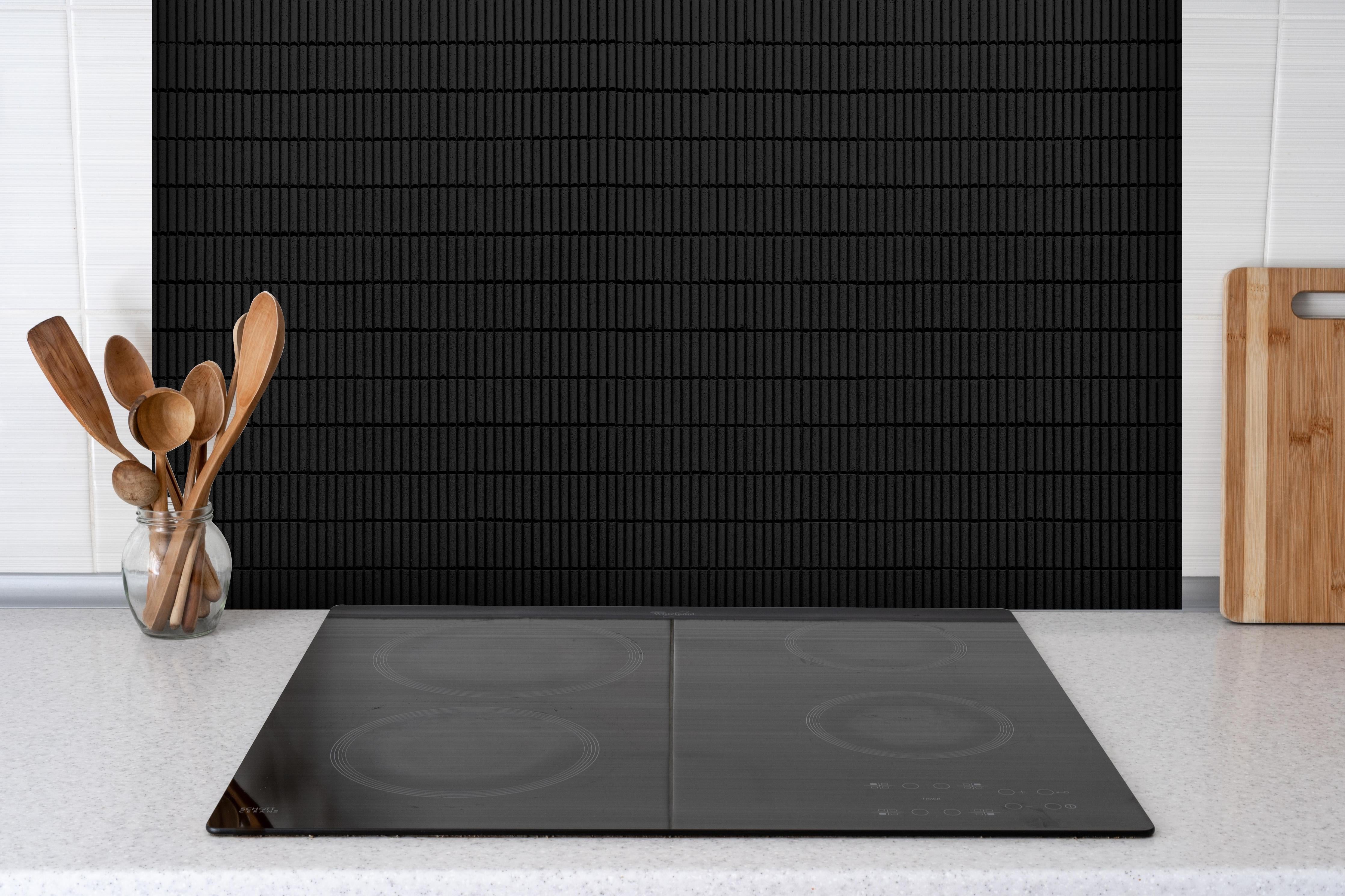 Spritzschutz - Schwarze geometrische Ziegeln hinter einem Cerankochfeld zwischen Holz-Kochutensilien