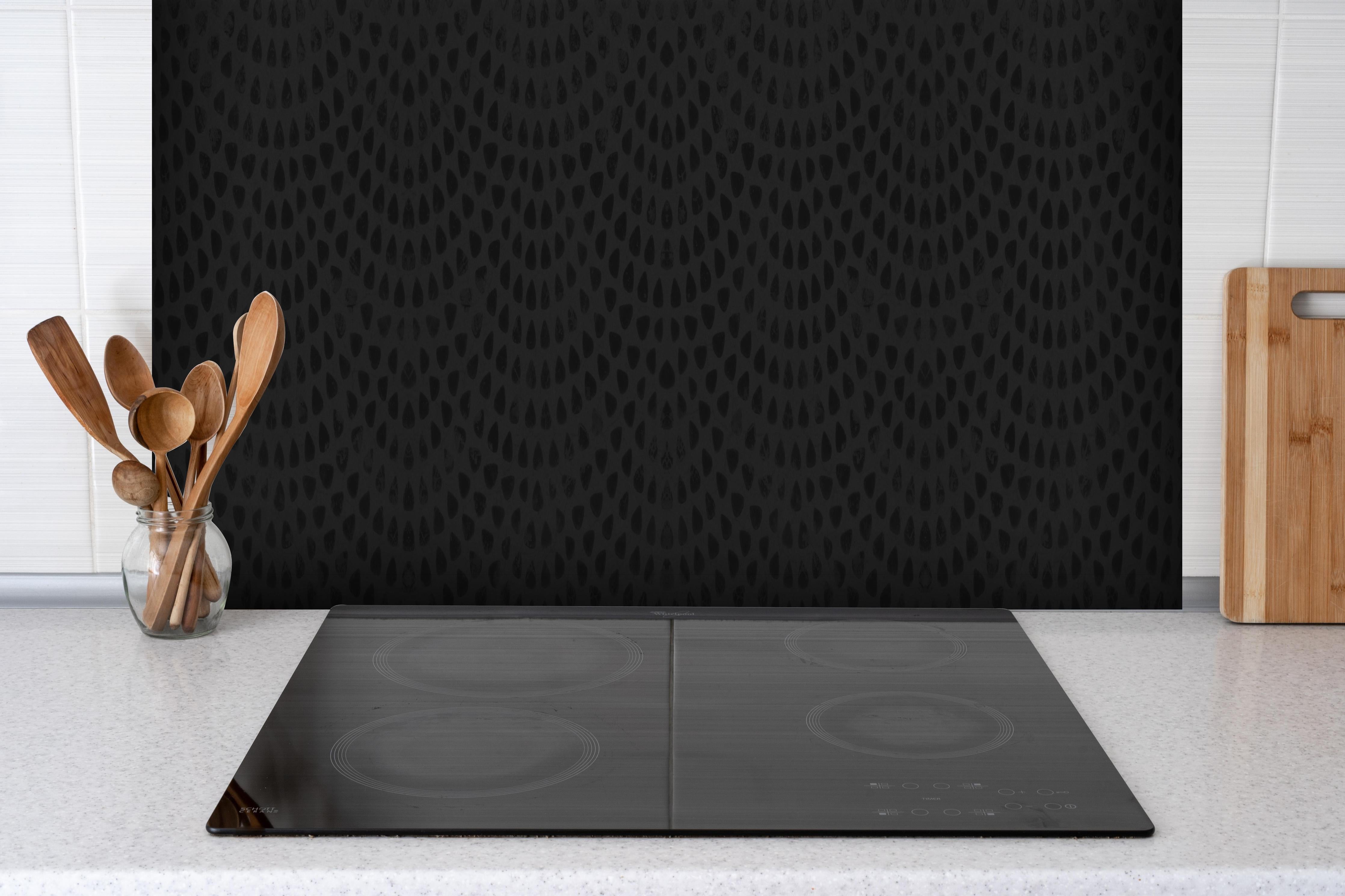 Spritzschutz - Schwarze geometrisches Stempelmuster hinter einem Cerankochfeld zwischen Holz-Kochutensilien