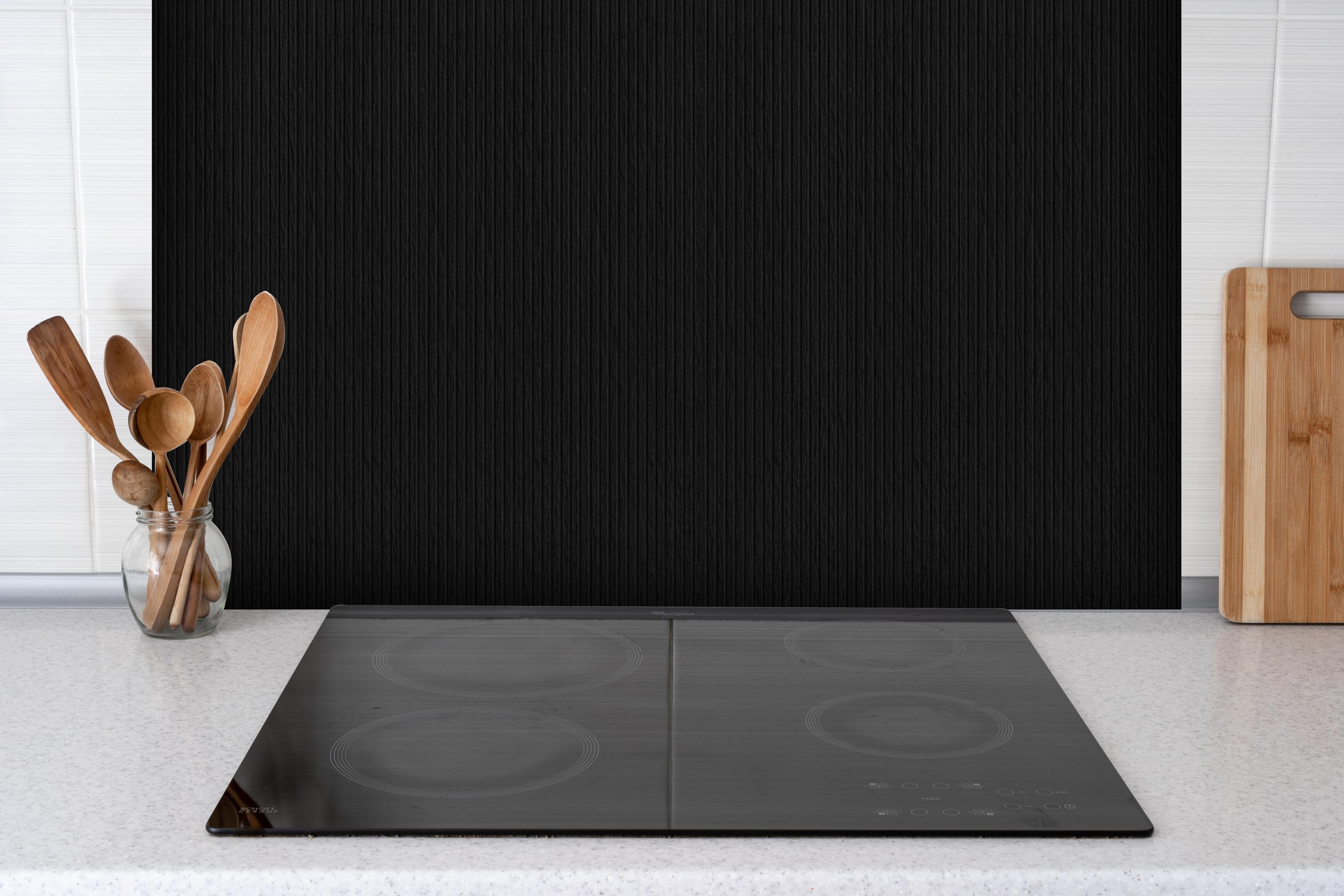 Spritzschutz - Schwarze moderne Zementwand mit Linien Muster hinter einem Cerankochfeld zwischen Holz-Kochutensilien