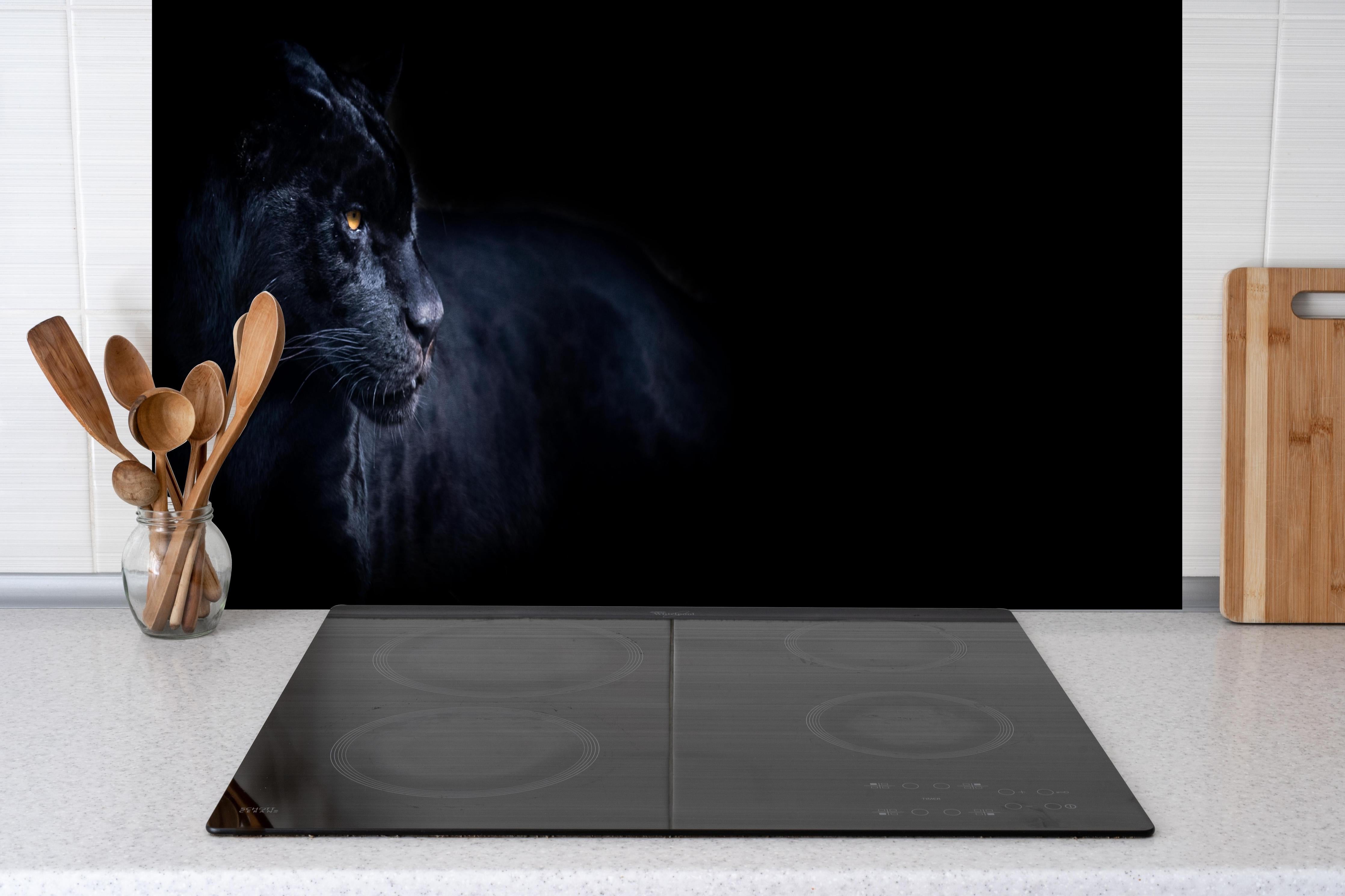 Spritzschutz - Schwarzen Panther mit schwarzem Hintergrund hinter einem Cerankochfeld zwischen Holz-Kochutensilien