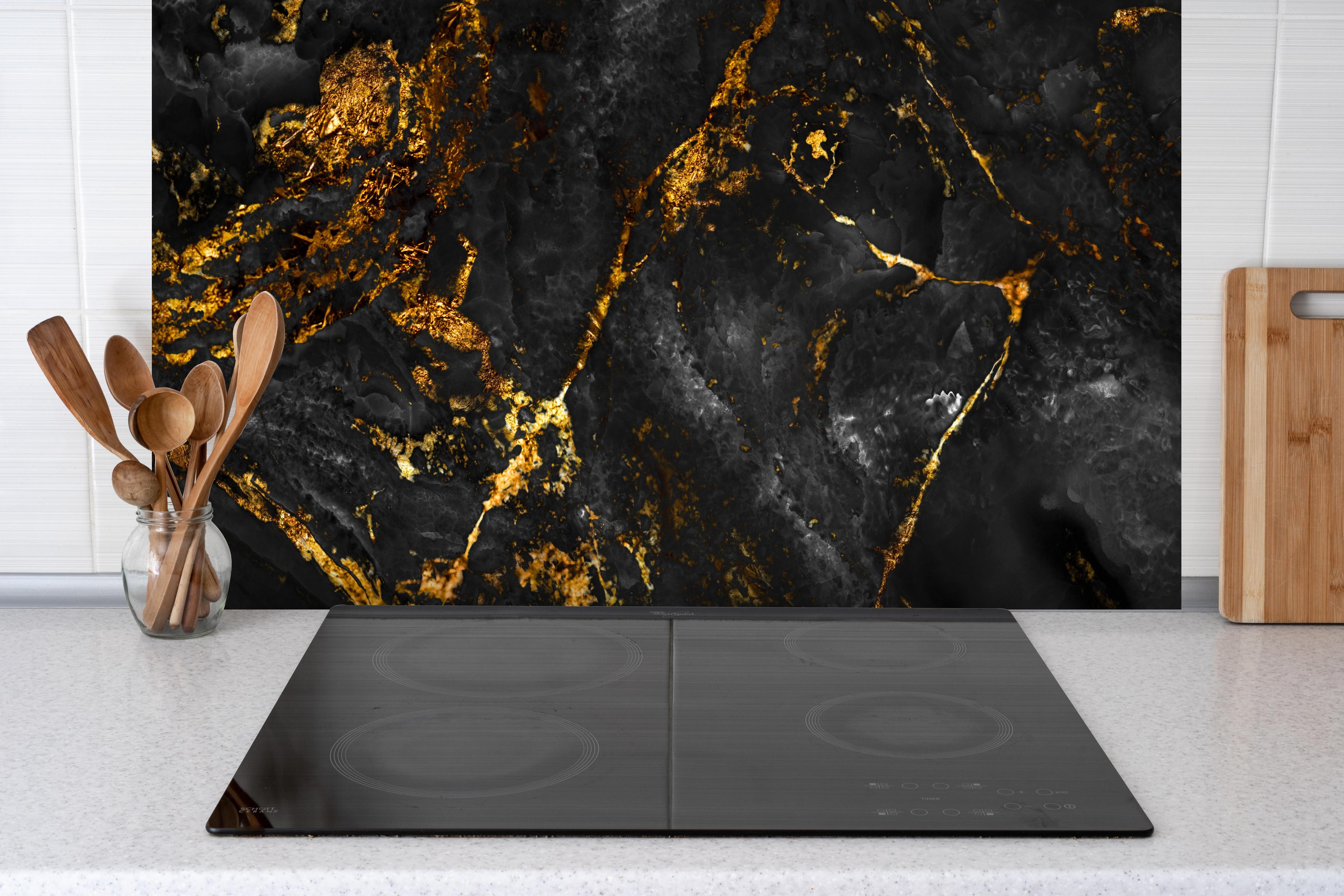 Spritzschutz - Schwarzer Marmor mit goldenen Adern hinter einem Cerankochfeld zwischen Holz-Kochutensilien