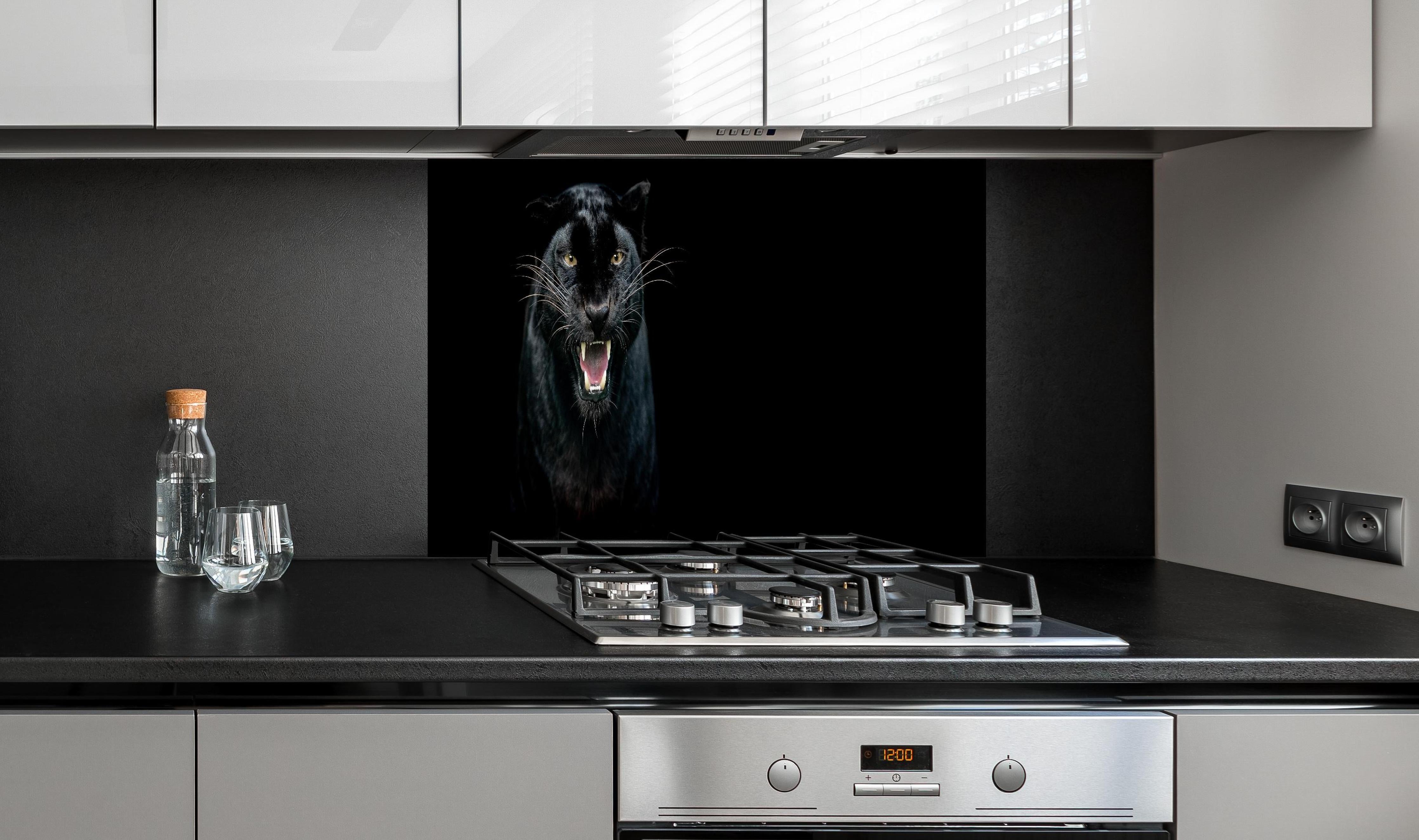Spritzschutz - Schwarzer Panther auf schwarzem Hintergrund hinter einem Cerankochfeld zwischen Holz-Kochutensilien