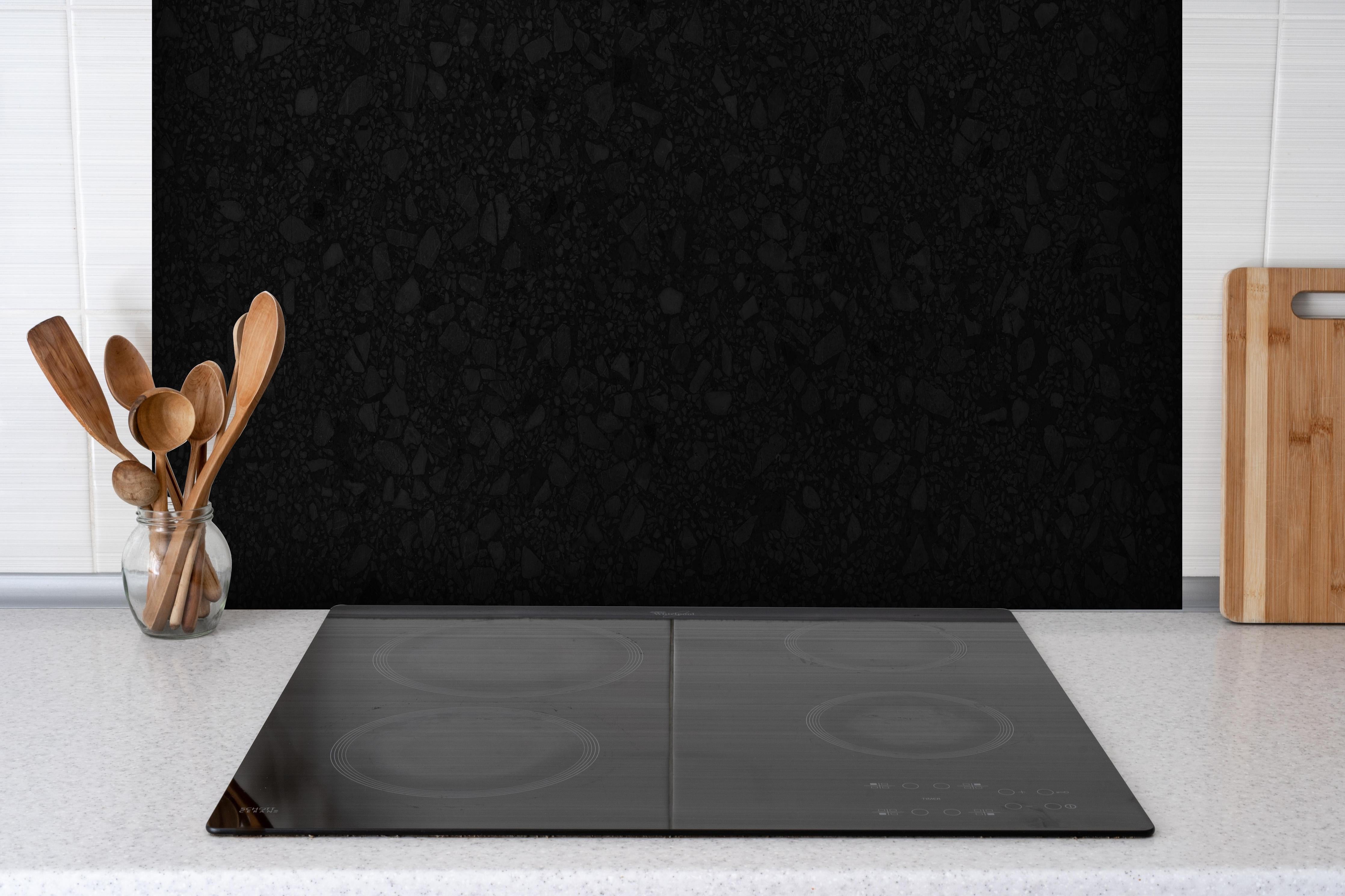 Spritzschutz - Schwarzer Sandstein hinter einem Cerankochfeld zwischen Holz-Kochutensilien