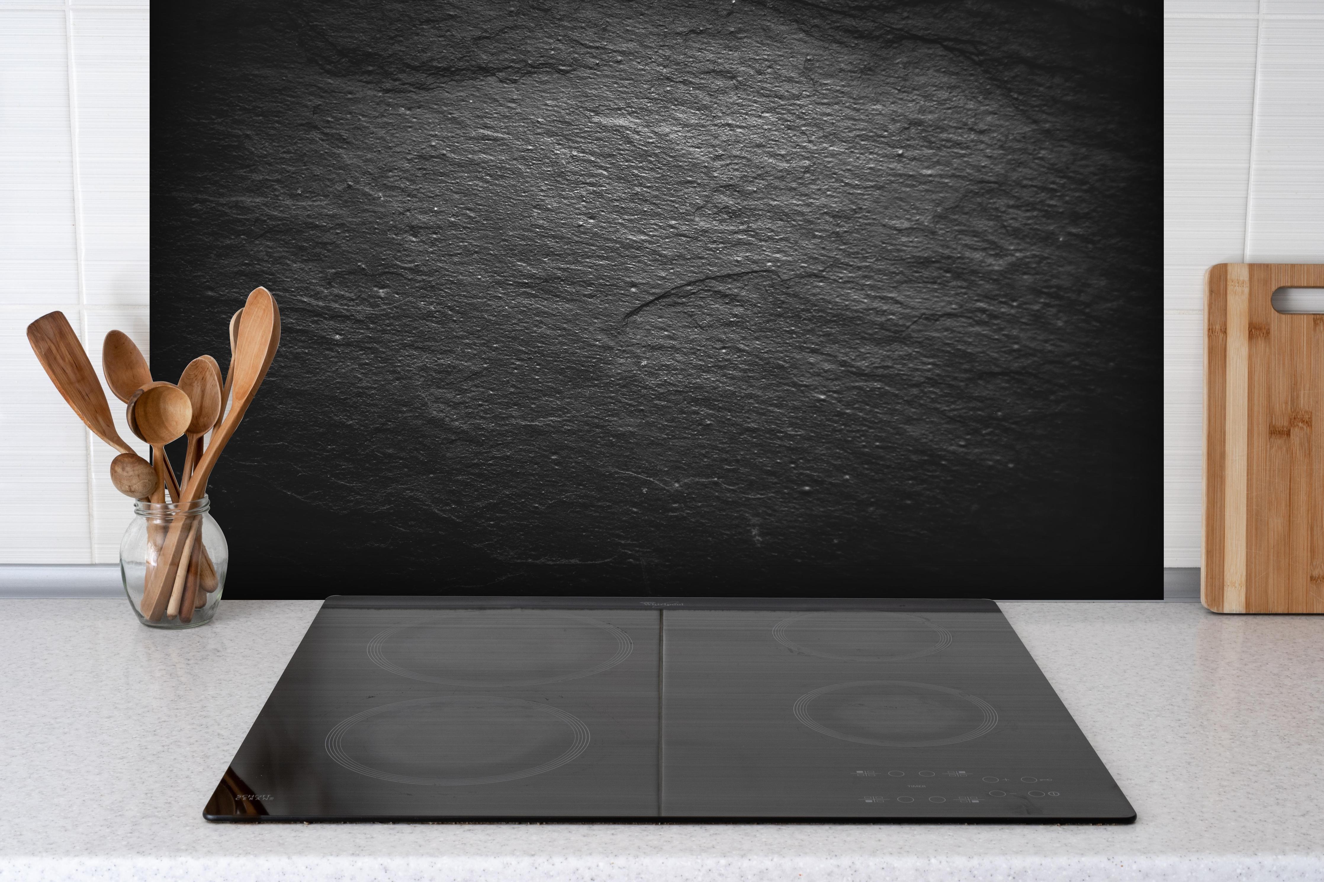 Spritzschutz - Schwarzer Schieferstein hinter einem Cerankochfeld zwischen Holz-Kochutensilien