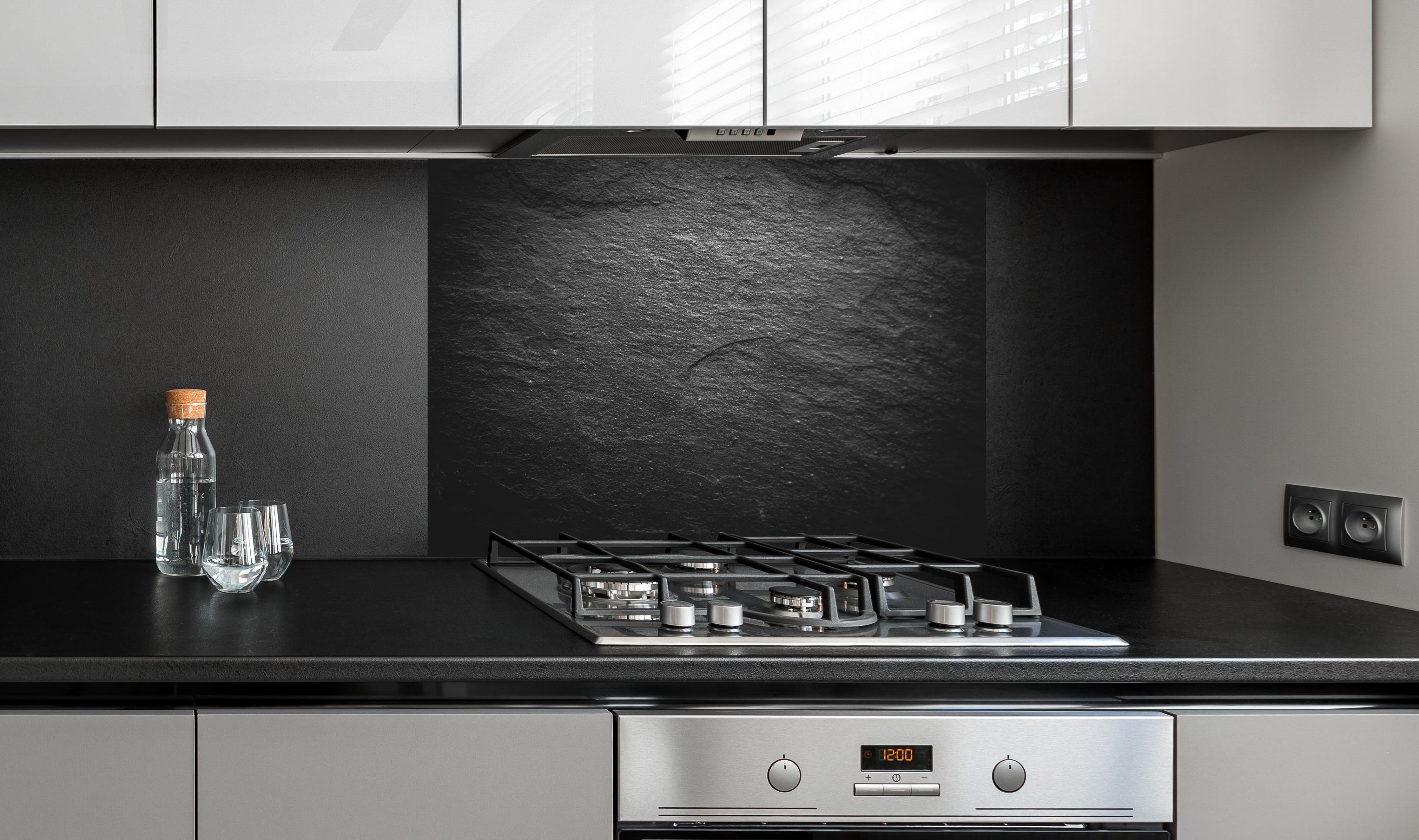 Spritzschutz - Schwarzer Schieferstein hinter einem Cerankochfeld zwischen Holz-Kochutensilien