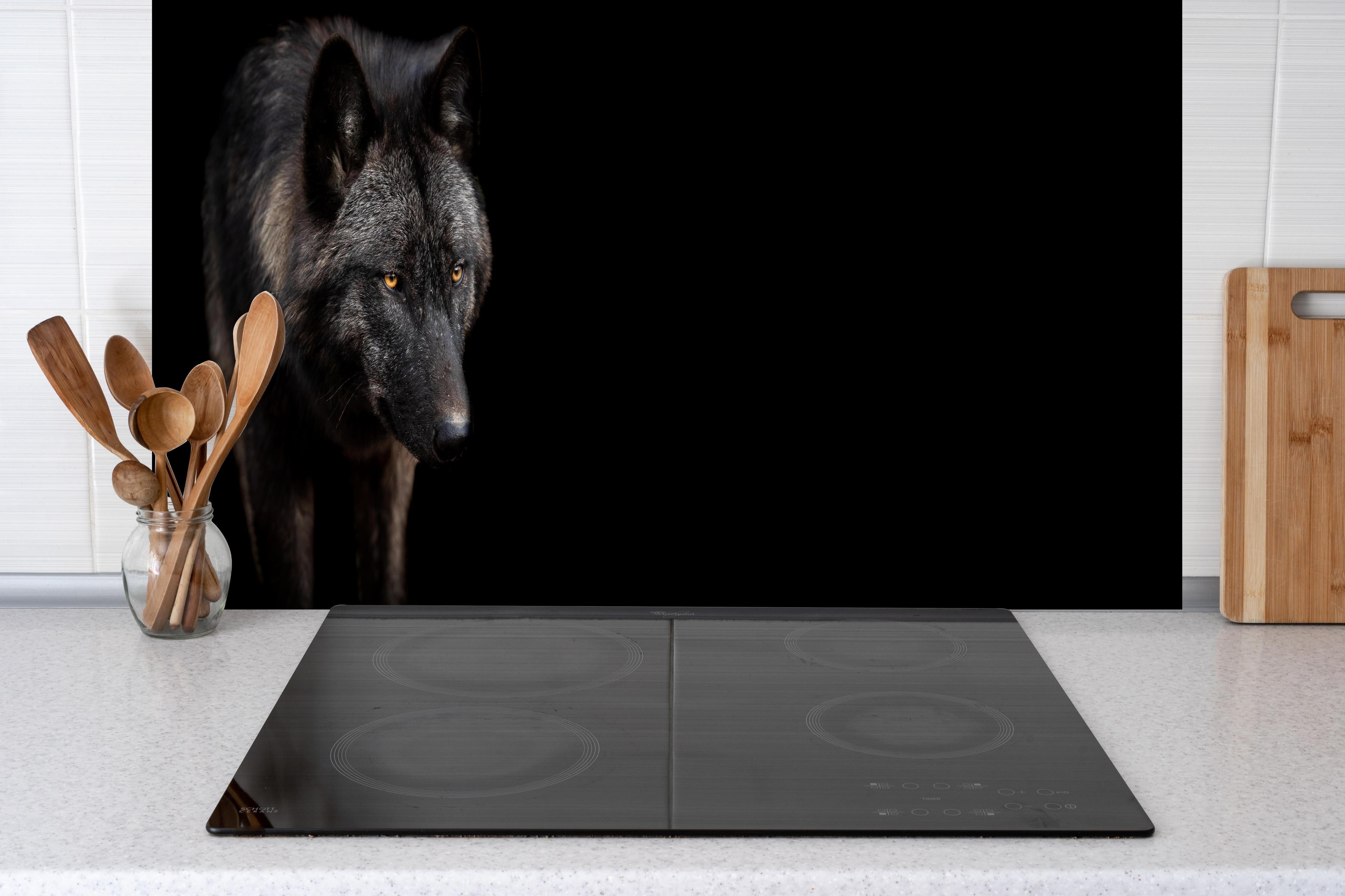 Spritzschutz - Schwarzer Wolf auf schwarzem Hintergrund hinter einem Cerankochfeld zwischen Holz-Kochutensilien