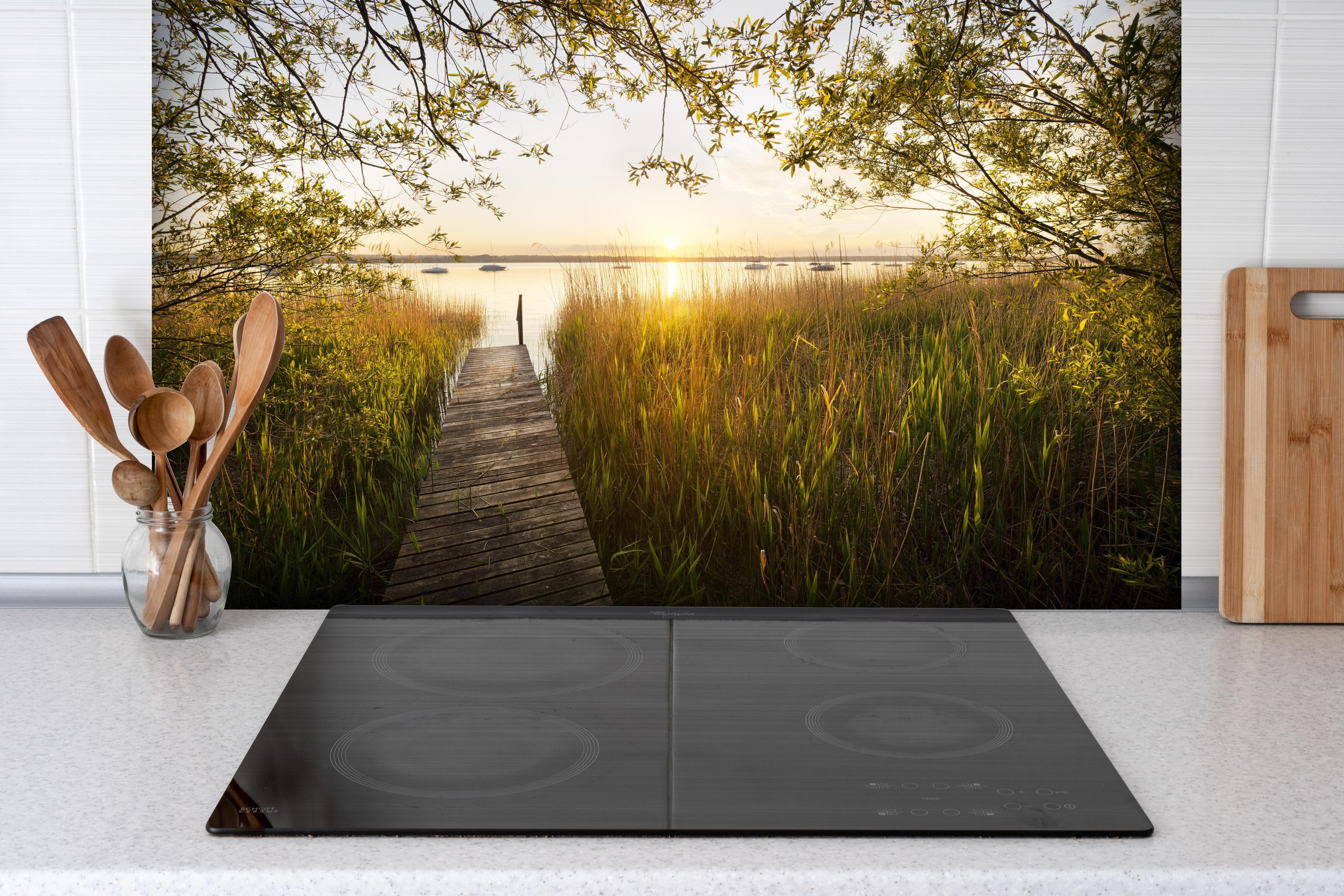 Spritzschutz - See in Bayern bei Sonnenuntergang hinter einem Cerankochfeld zwischen Holz-Kochutensilien