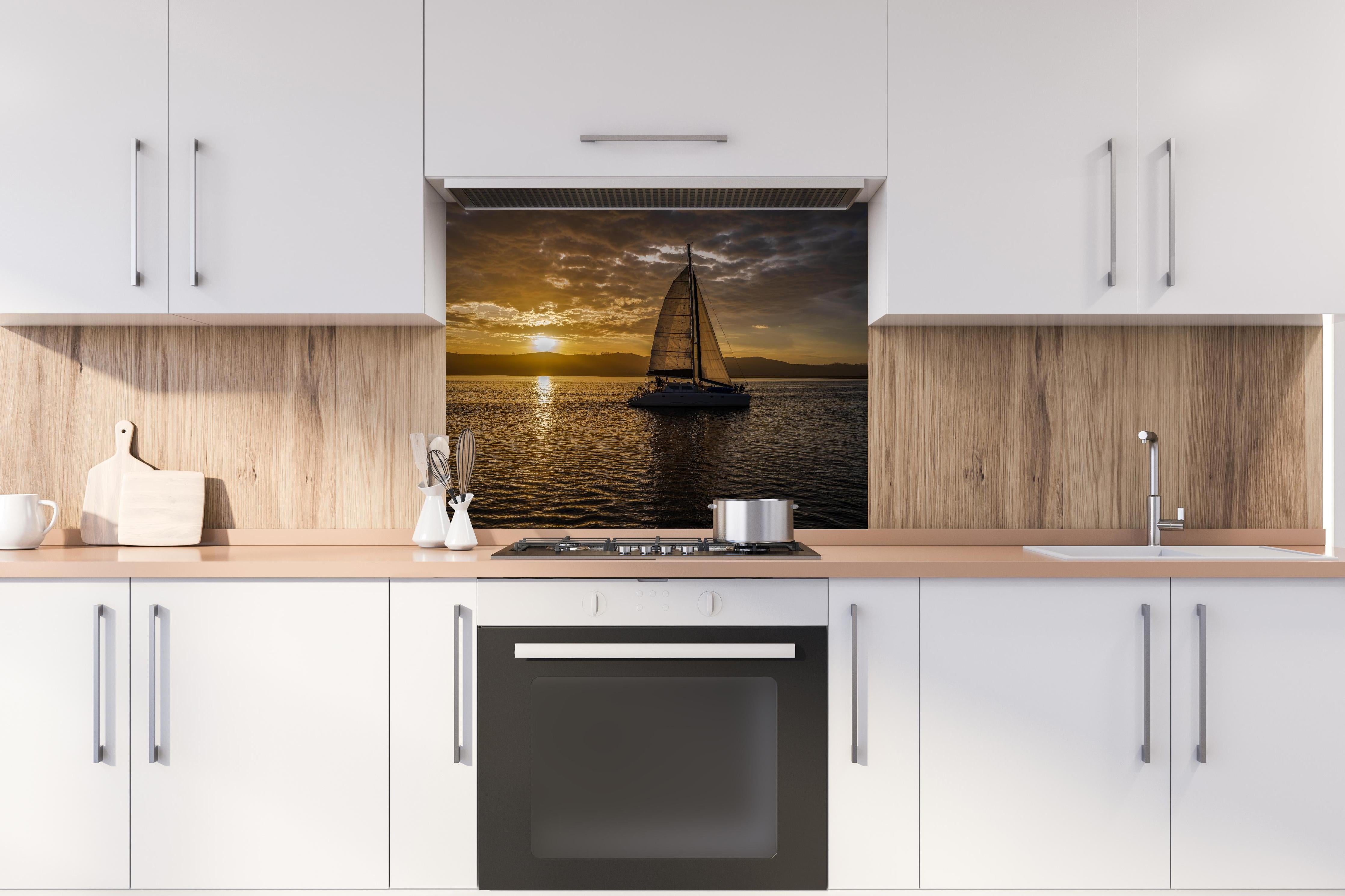 Spritzschutz - Segelboot bei Sonnenuntergang in der Lagune von Knysna hinter einem Cerankochfeld zwischen Holz-Kochutensilien