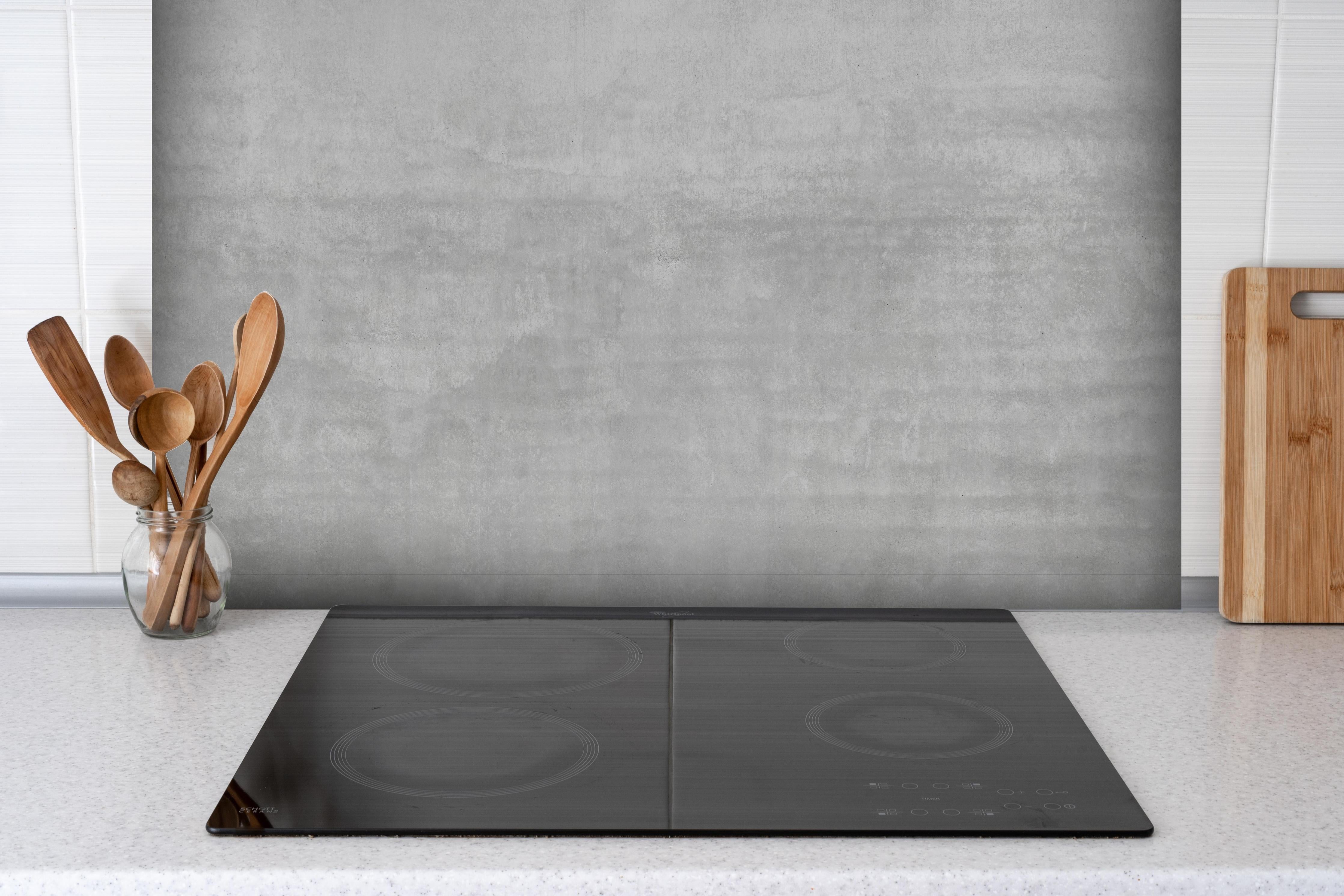 Spritzschutz - Sicht-Beton Textur hinter einem Cerankochfeld zwischen Holz-Kochutensilien