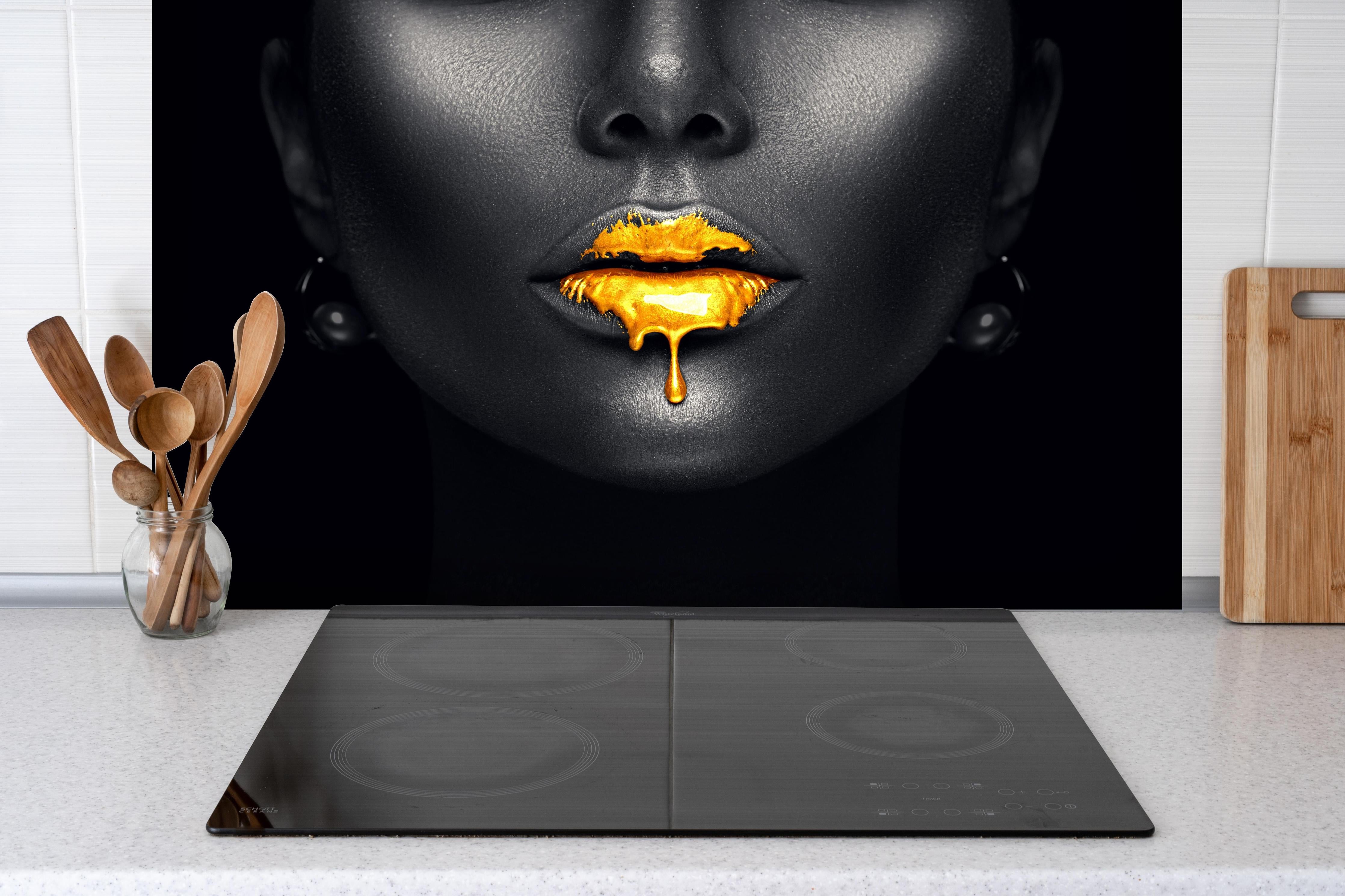 Spritzschutz - Sinnliche Lippen mit Goldtropfen hinter einem Cerankochfeld zwischen Holz-Kochutensilien