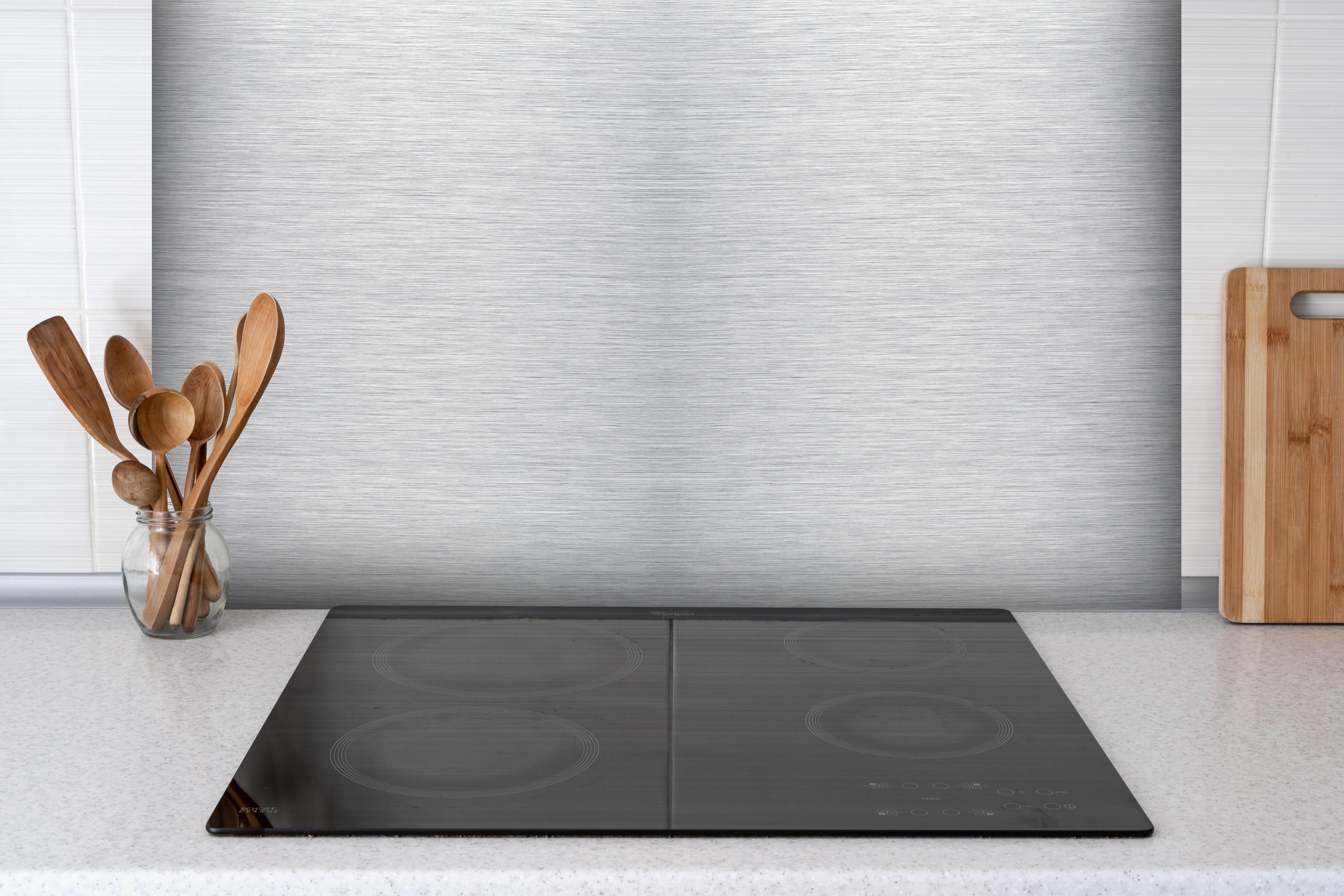 Spritzschutz - Skip hinter einem Cerankochfeld zwischen Holz-Kochutensilien