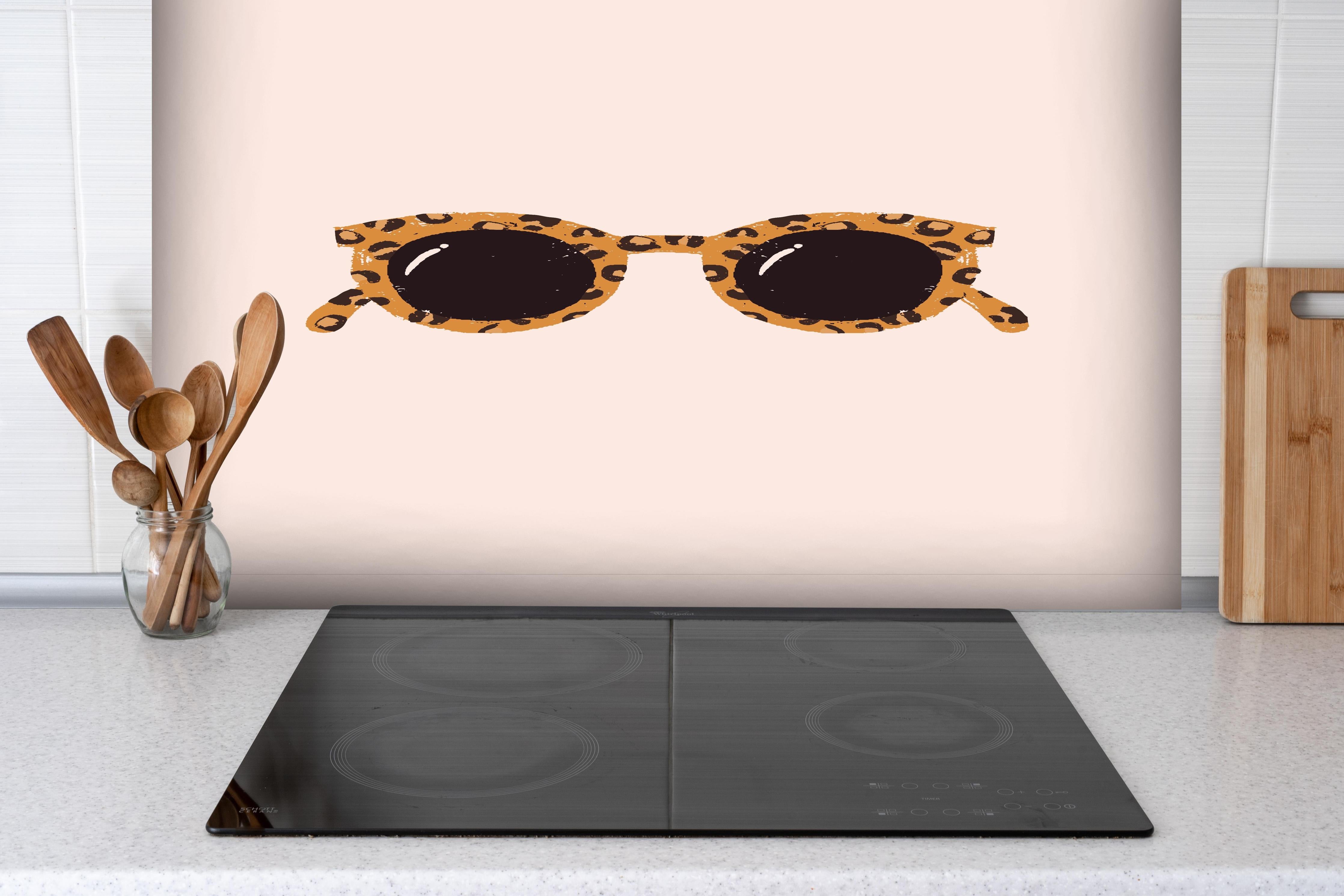 Spritzschutz - Sonnenbrille - Leopardenmuster hinter einem Cerankochfeld zwischen Holz-Kochutensilien