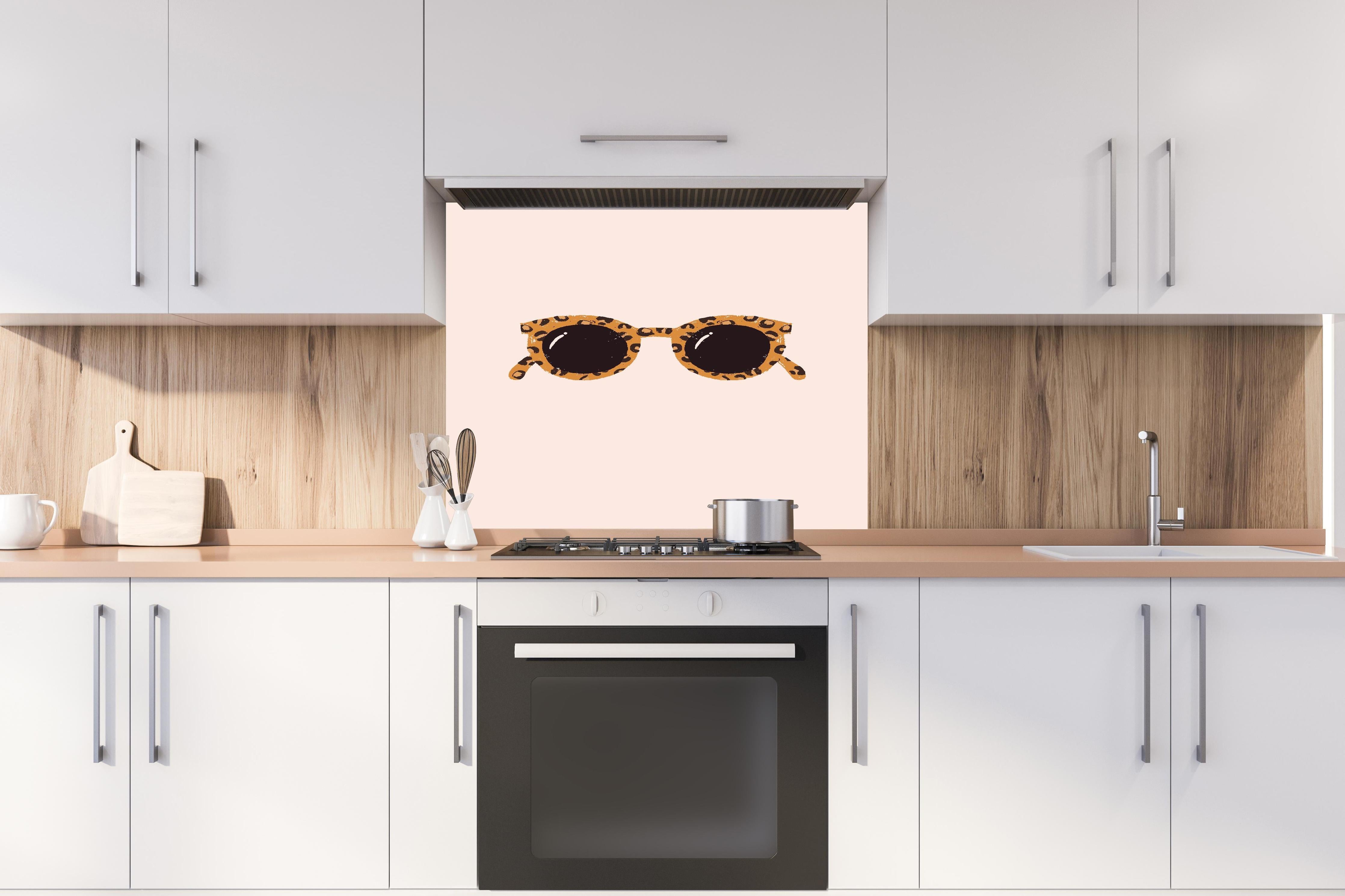 Spritzschutz - Sonnenbrille - Leopardenmuster hinter einem Cerankochfeld zwischen Holz-Kochutensilien