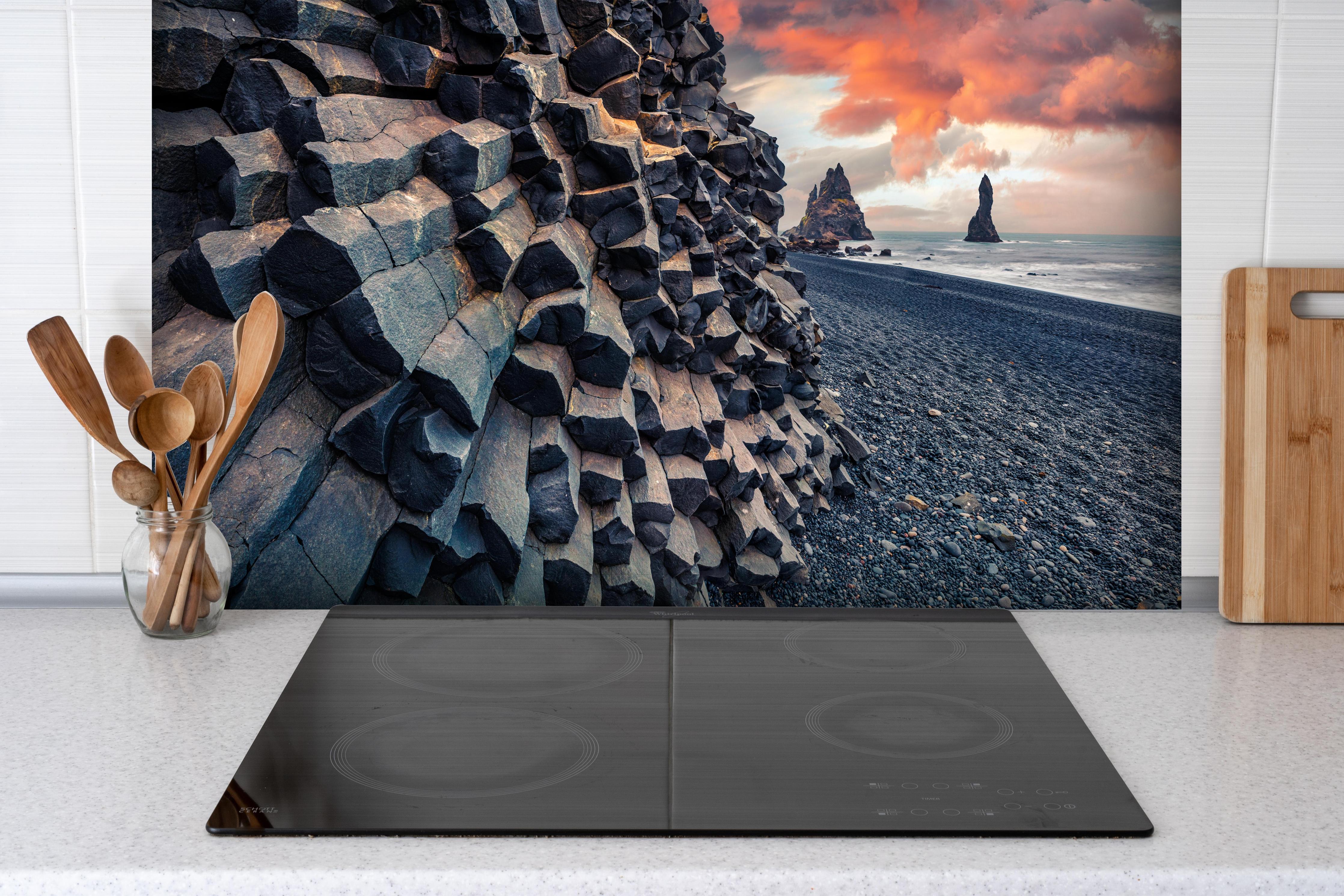 Spritzschutz - Sonnenuntergang - Reynisdrangar, Atlantischer Ozean hinter einem Cerankochfeld zwischen Holz-Kochutensilien