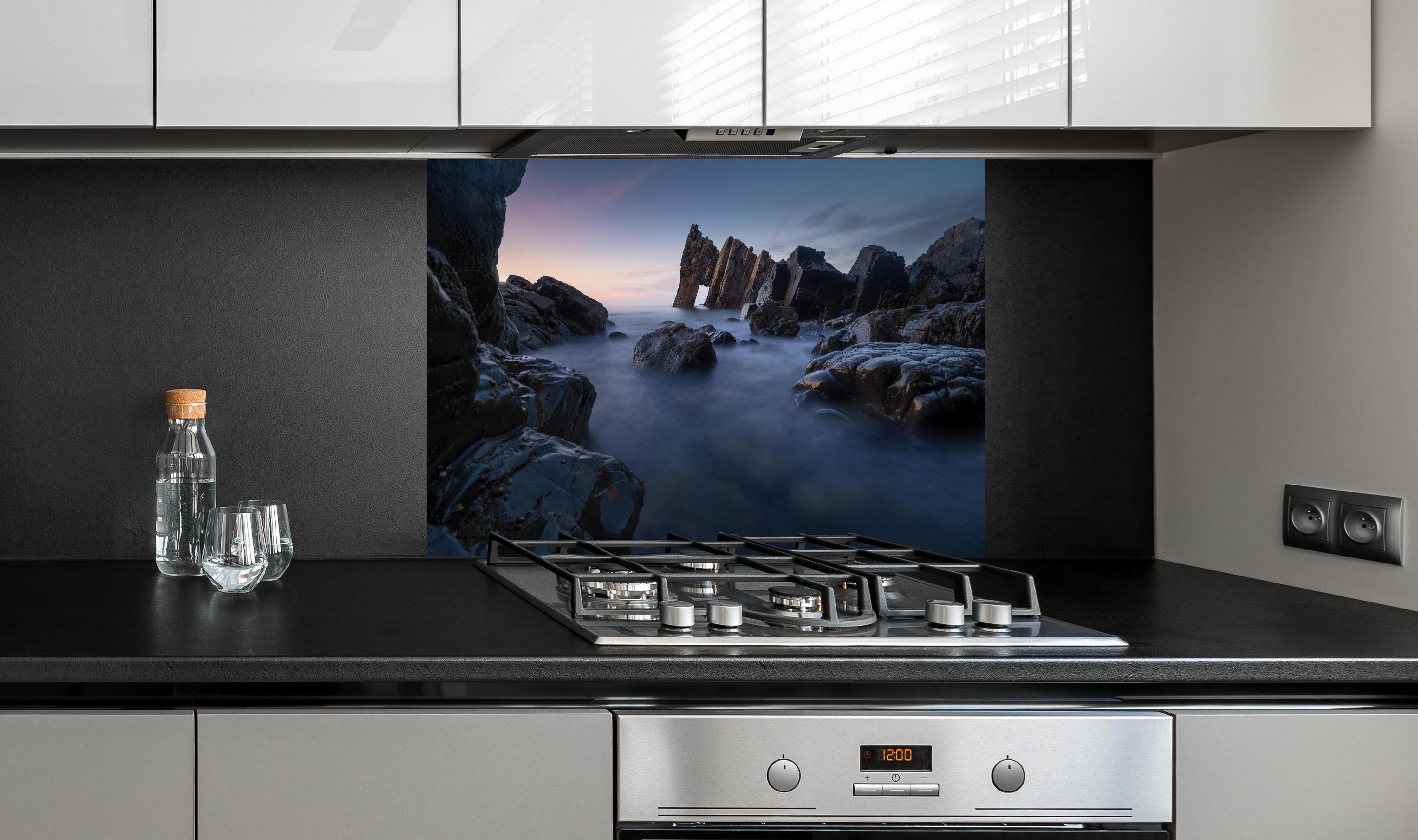 Spritzschutz - Sonnenuntergang am felsigen Meeresufer hinter einem Cerankochfeld zwischen Holz-Kochutensilien