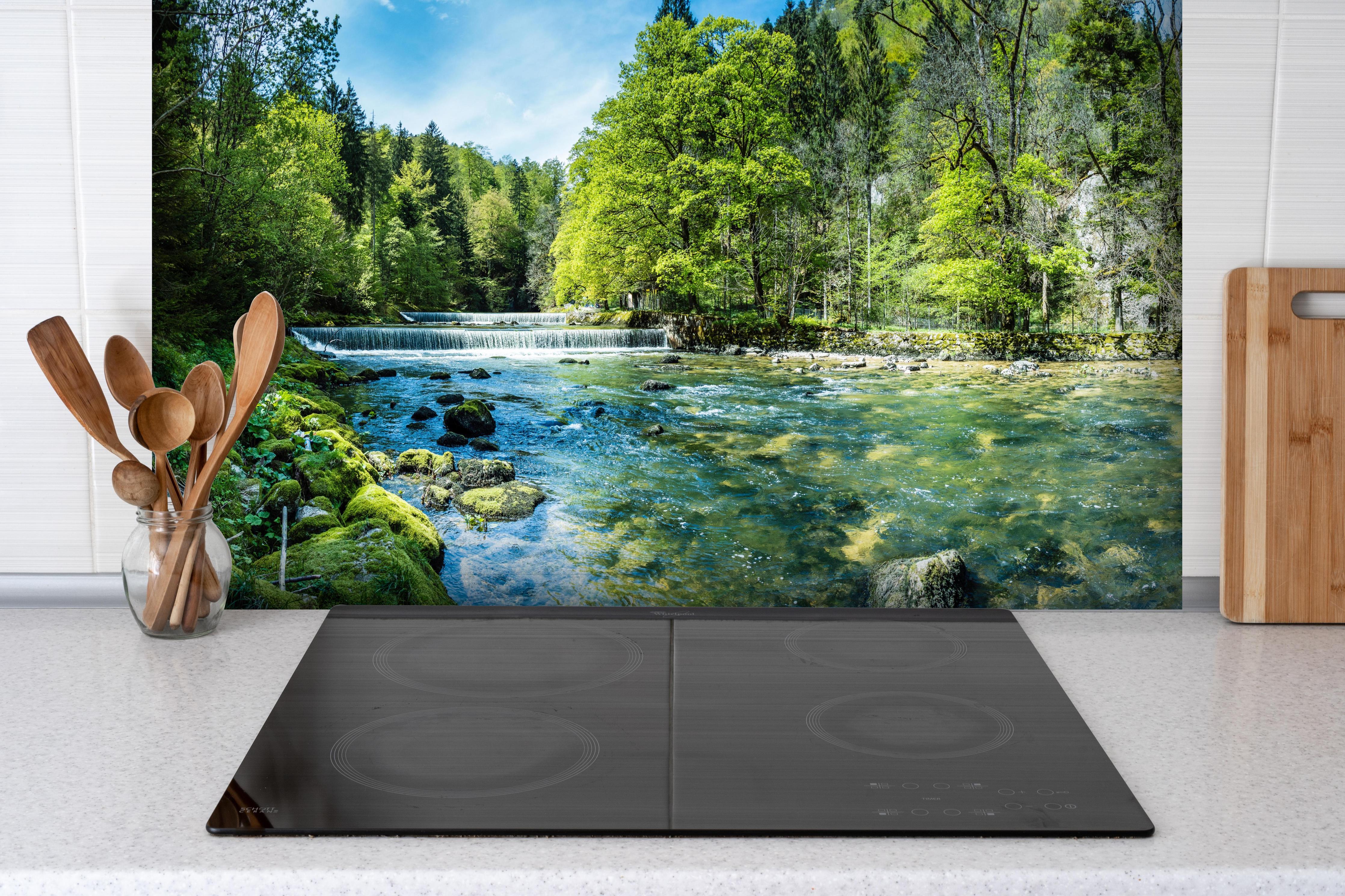 Spritzschutz - Sonnige Flusslandschaft in der Schweiz hinter einem Cerankochfeld zwischen Holz-Kochutensilien