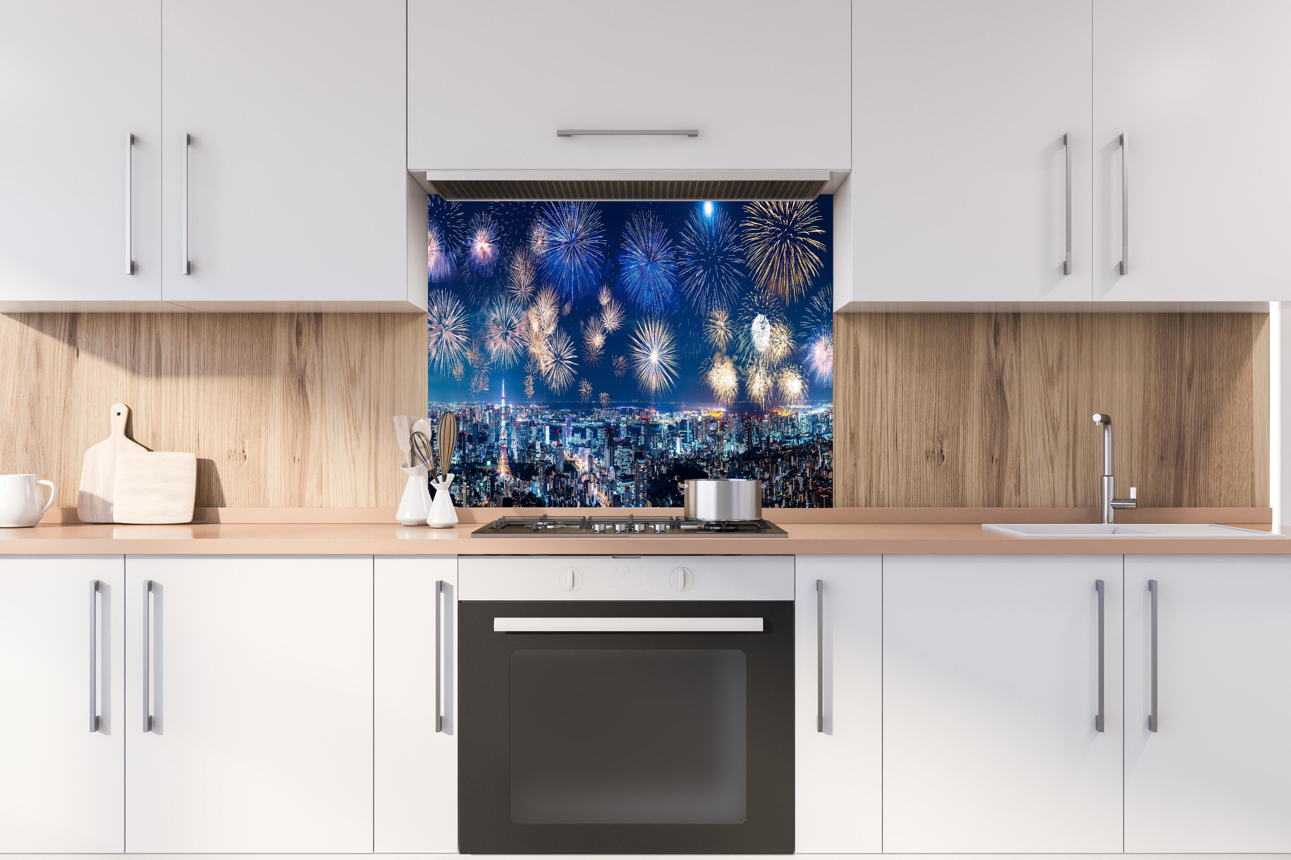 Spritzschutz - Spektakuläres Feuerwerk über Stadt bei Nacht hinter einem Cerankochfeld zwischen Holz-Kochutensilien