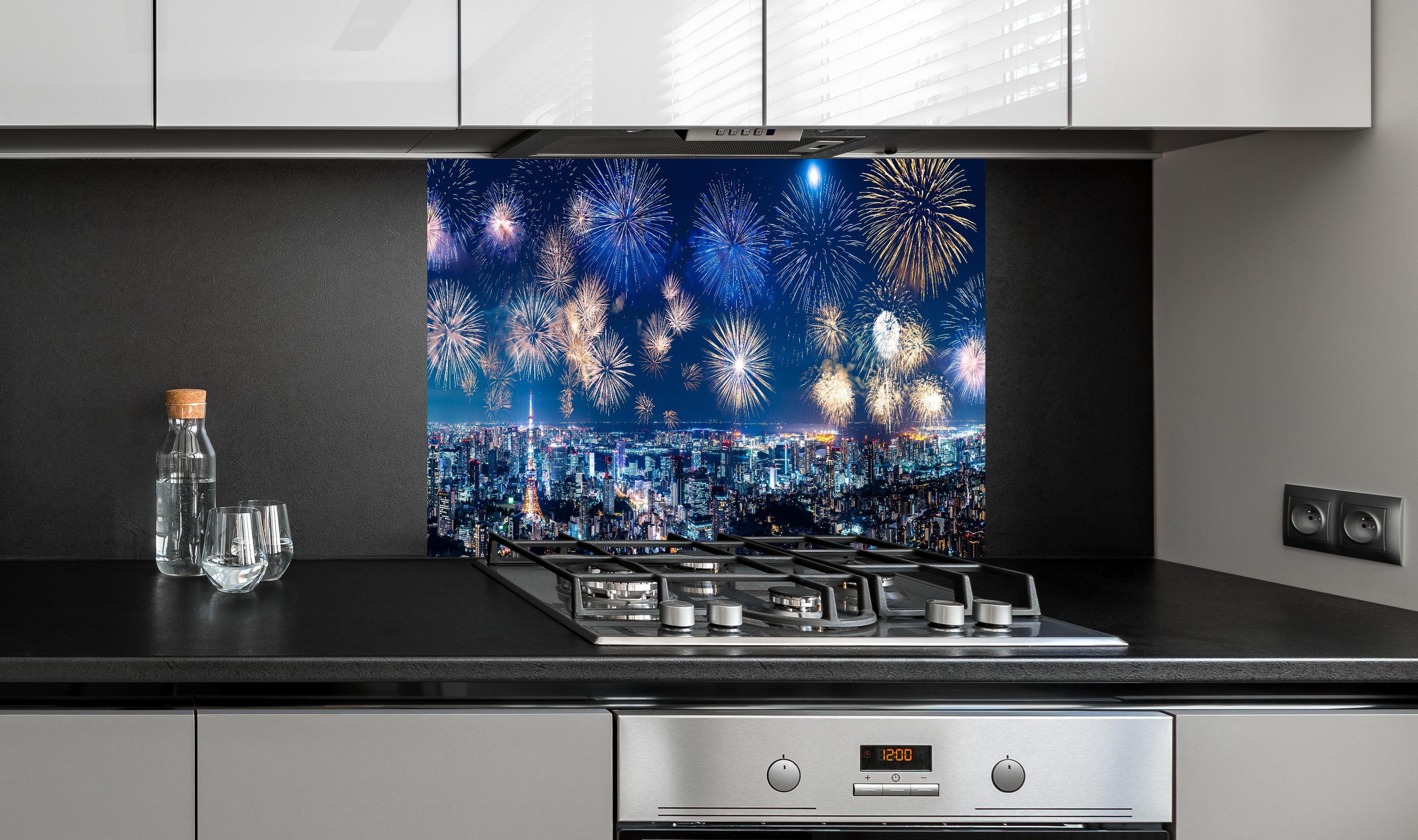 Spritzschutz - Spektakuläres Feuerwerk über Stadt bei Nacht hinter einem Cerankochfeld zwischen Holz-Kochutensilien